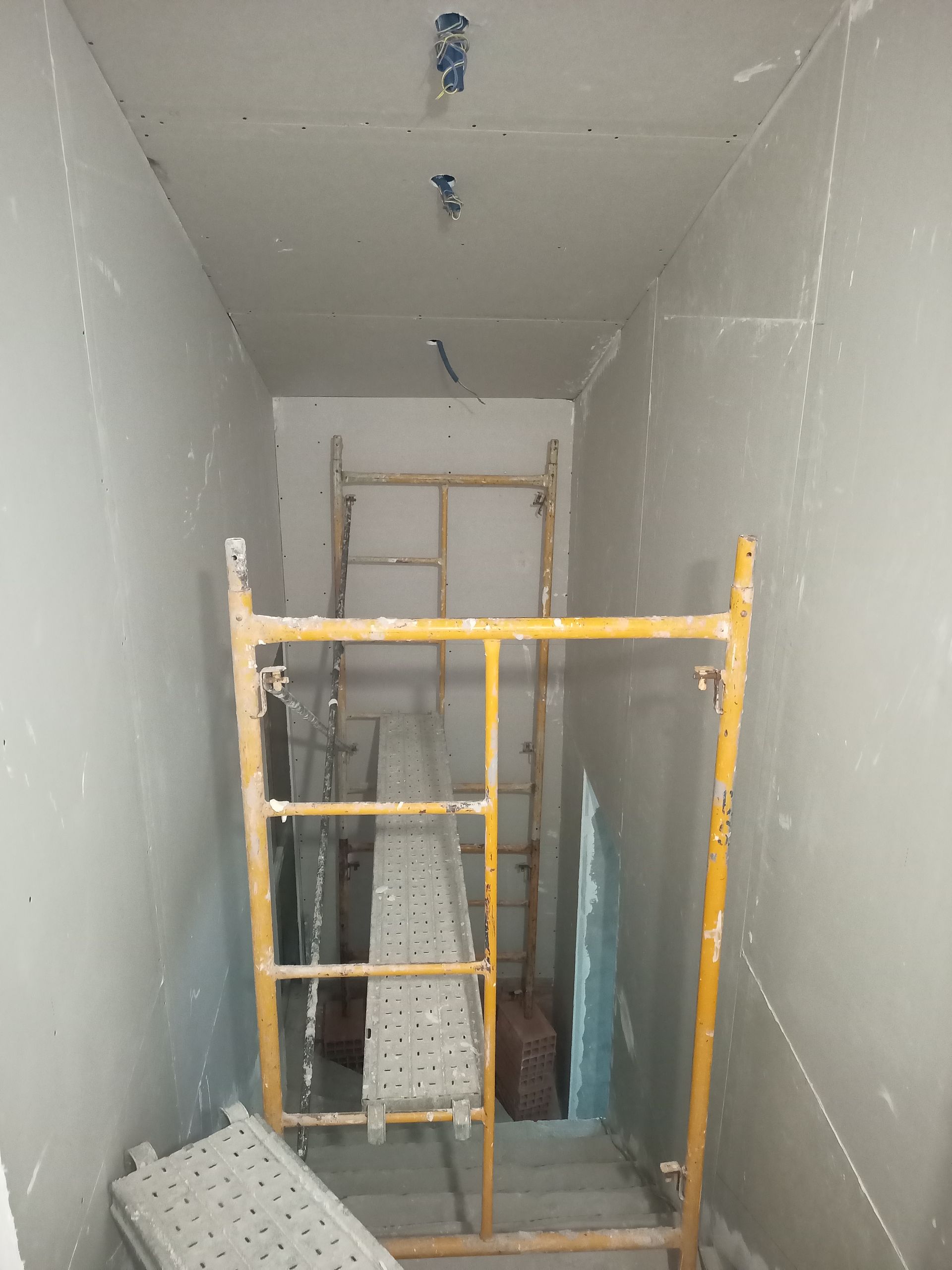 Canteiro de obras: Corredor estreito com andaimes; instalação de drywall.