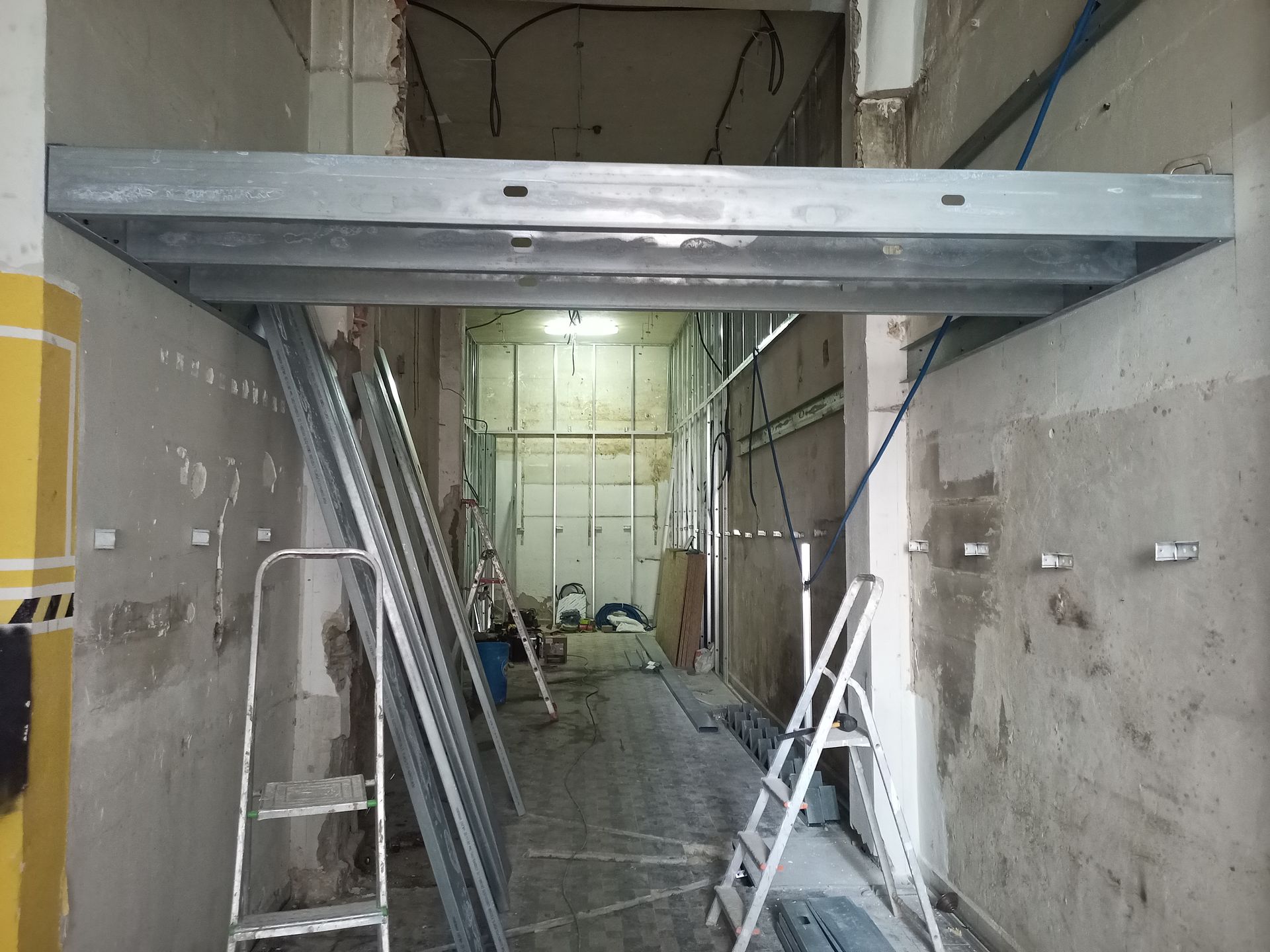 Estrutura metálica instalada ao longo de um corredor durante a construção. Ferramentas, escadas e paredes expostas são visíveis.