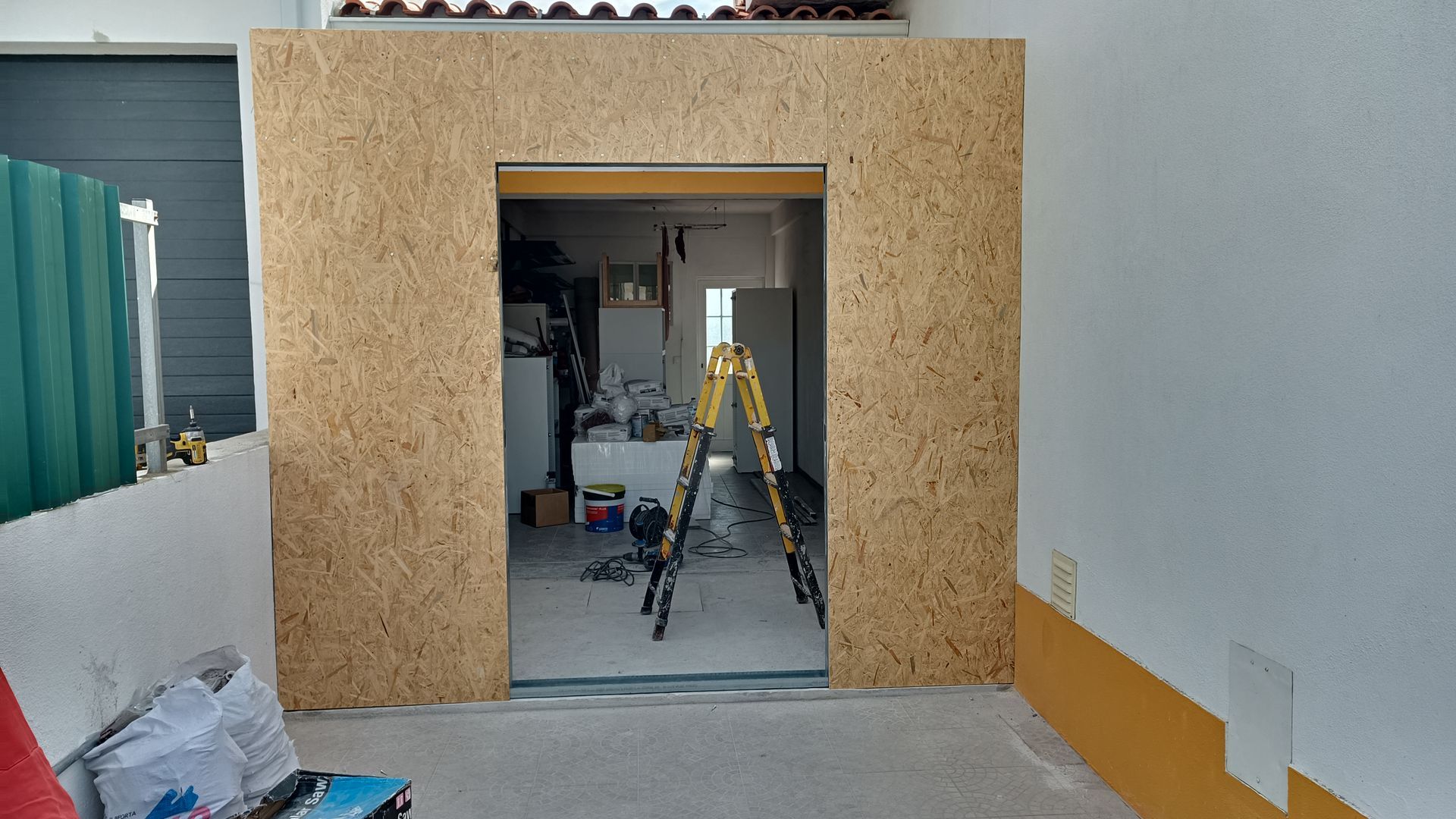 Uma porta em construção, emoldurada por painéis OSB marrom-claros, dá acesso a um interior desorganizado.