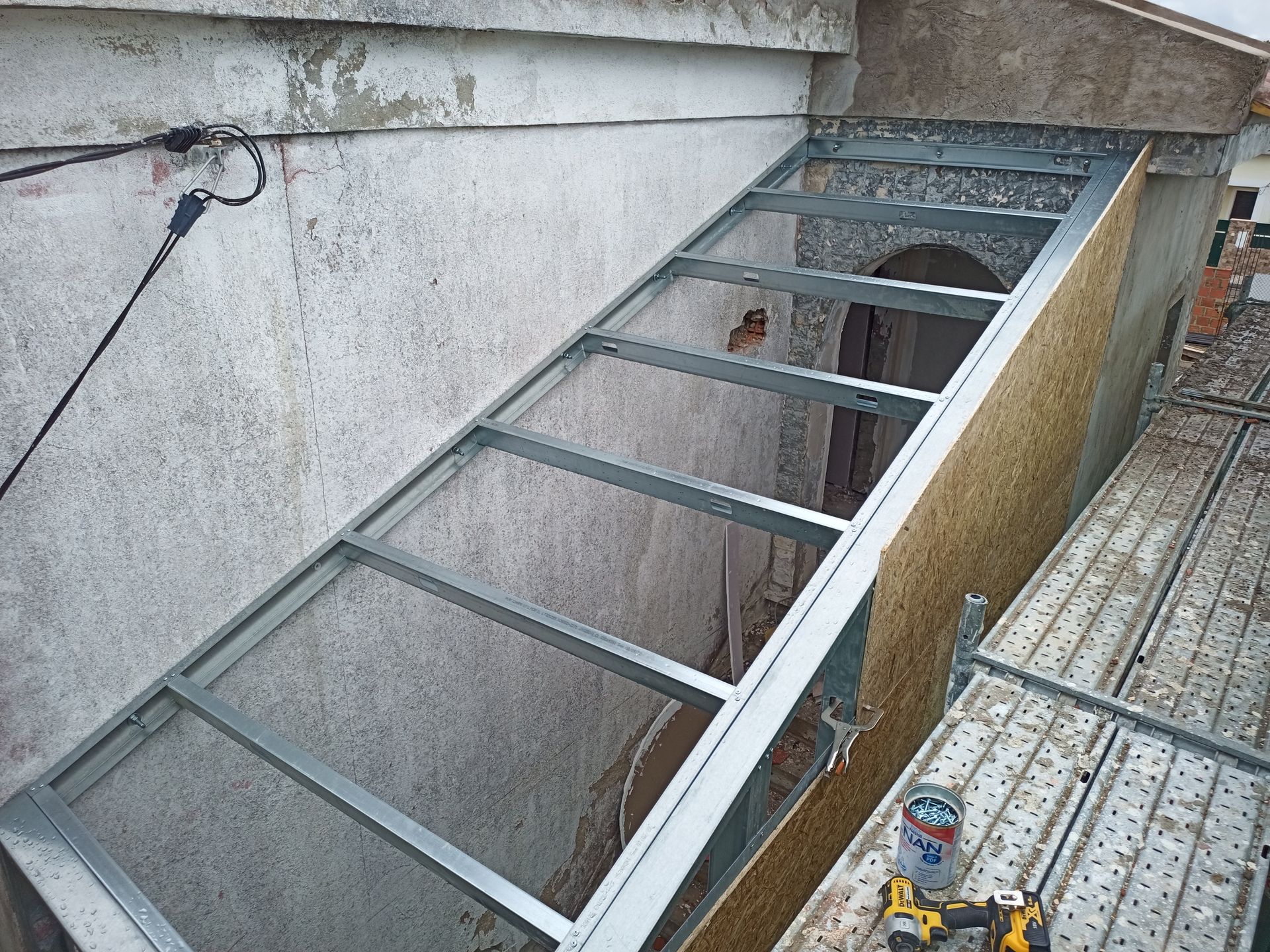 Estrutura metálica fixada a um edifício, possivelmente para uma rampa ou cobertura, durante a construção.