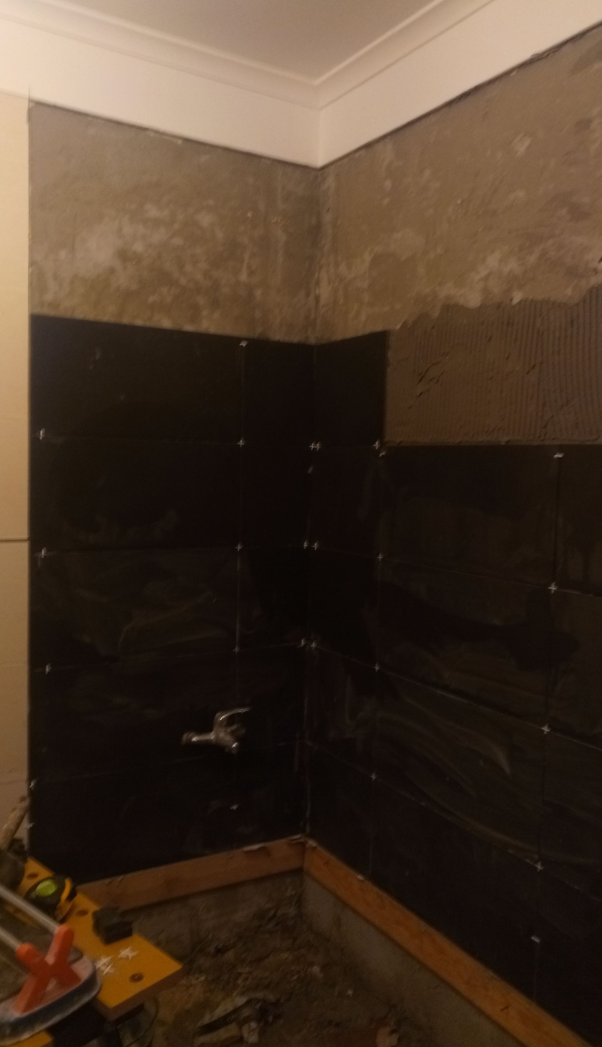 Parede do banheiro com azulejos pretos parcialmente instalados, ao redor do chuveiro.