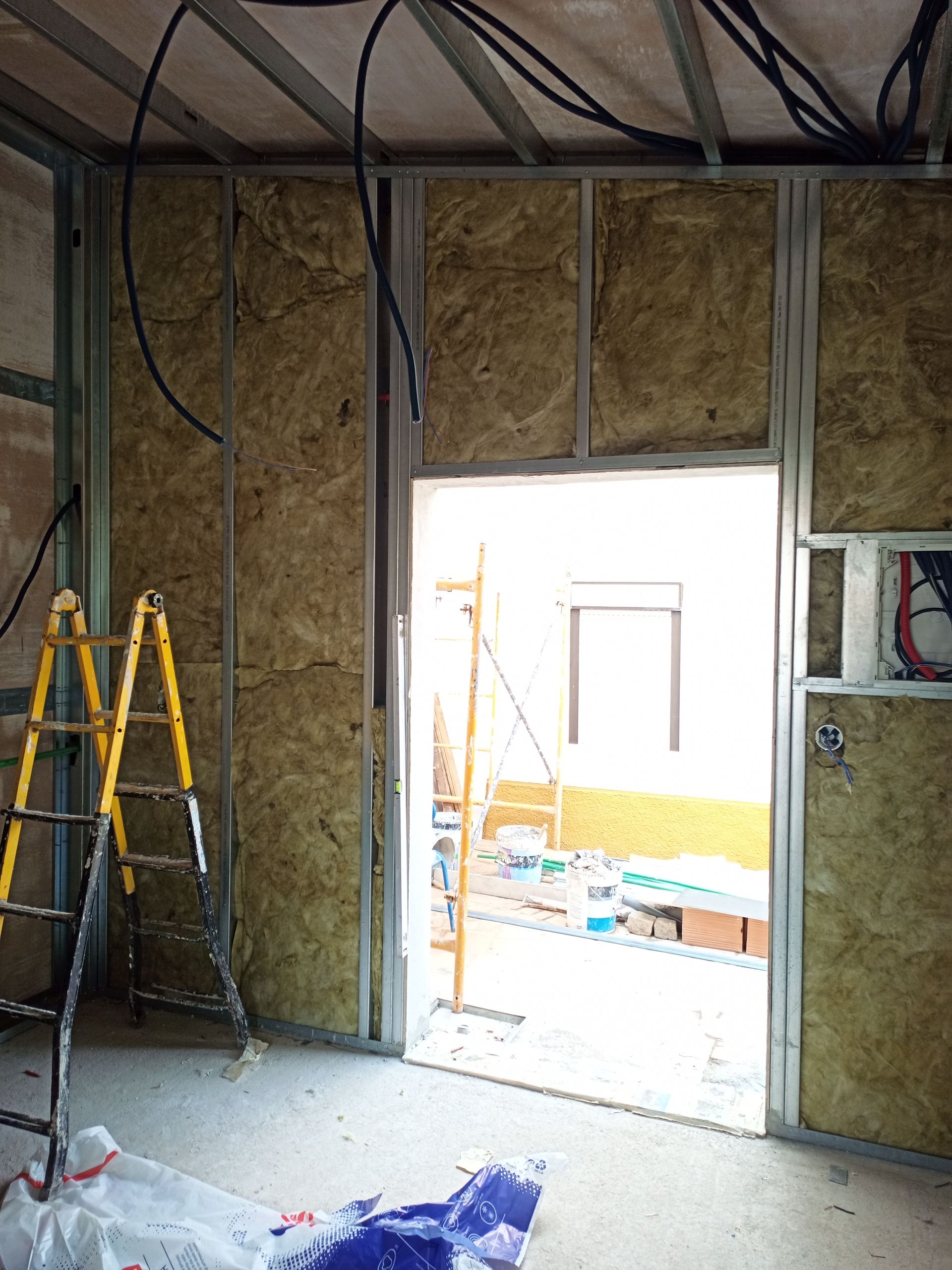 Construção interna: paredes com estrutura de aço e isolamento, porta, escada amarela, fiação elétrica.