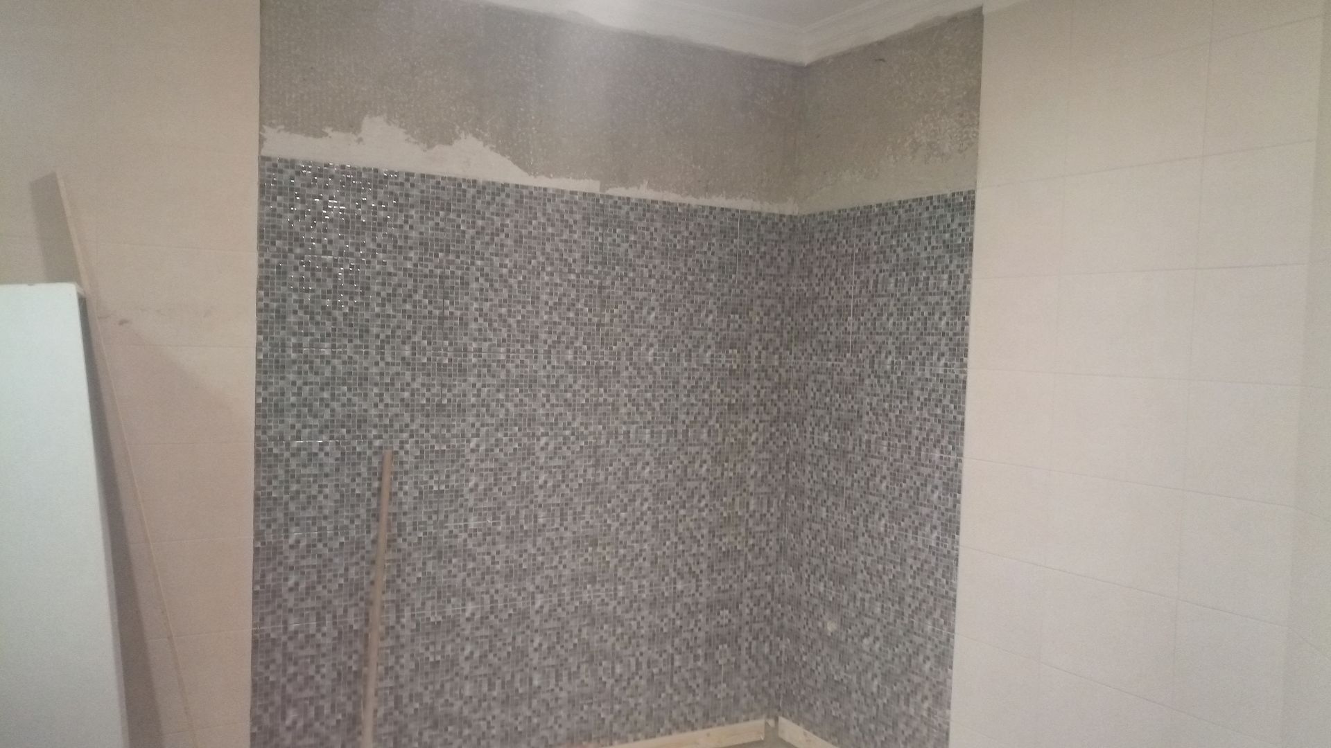 Canto de parede texturizada em cinza, parcialmente rebocado, cercado por paredes lisas em tom bege.