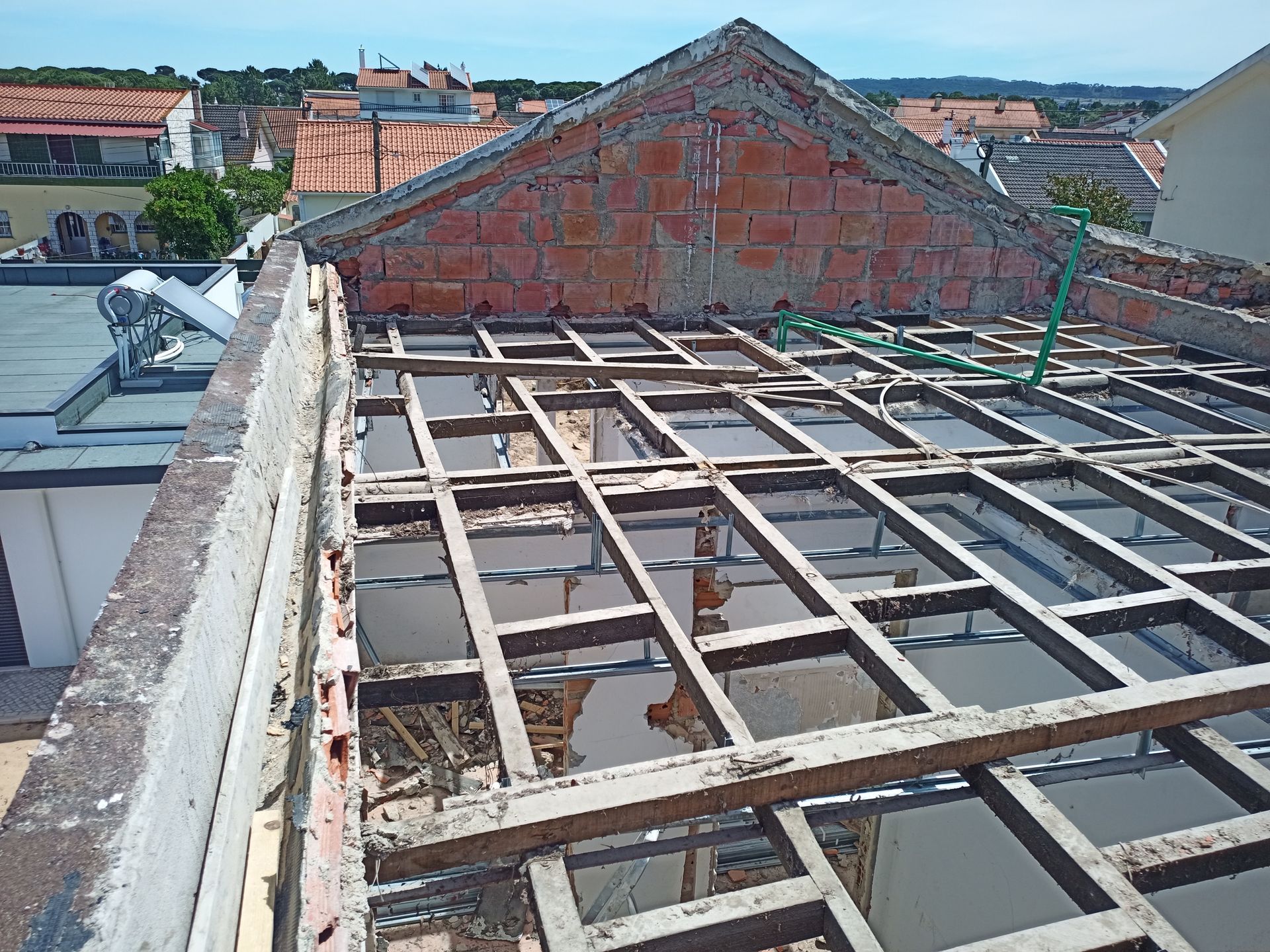 Telhado parcialmente construído, mostrando vigas de madeira e alvenaria, em um edifício com vista para a cidade.