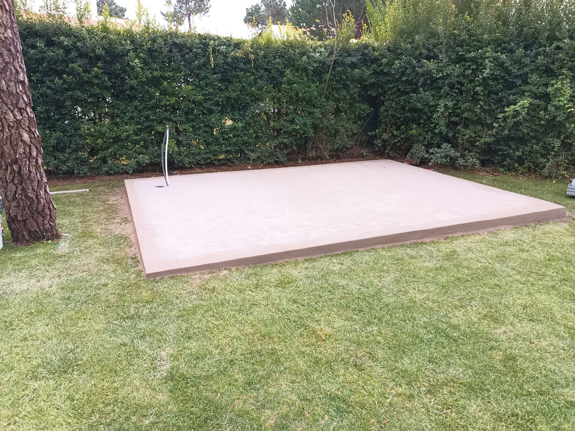 Uma plataforma de concreto com um cano, cercada por grama e uma cerca viva.