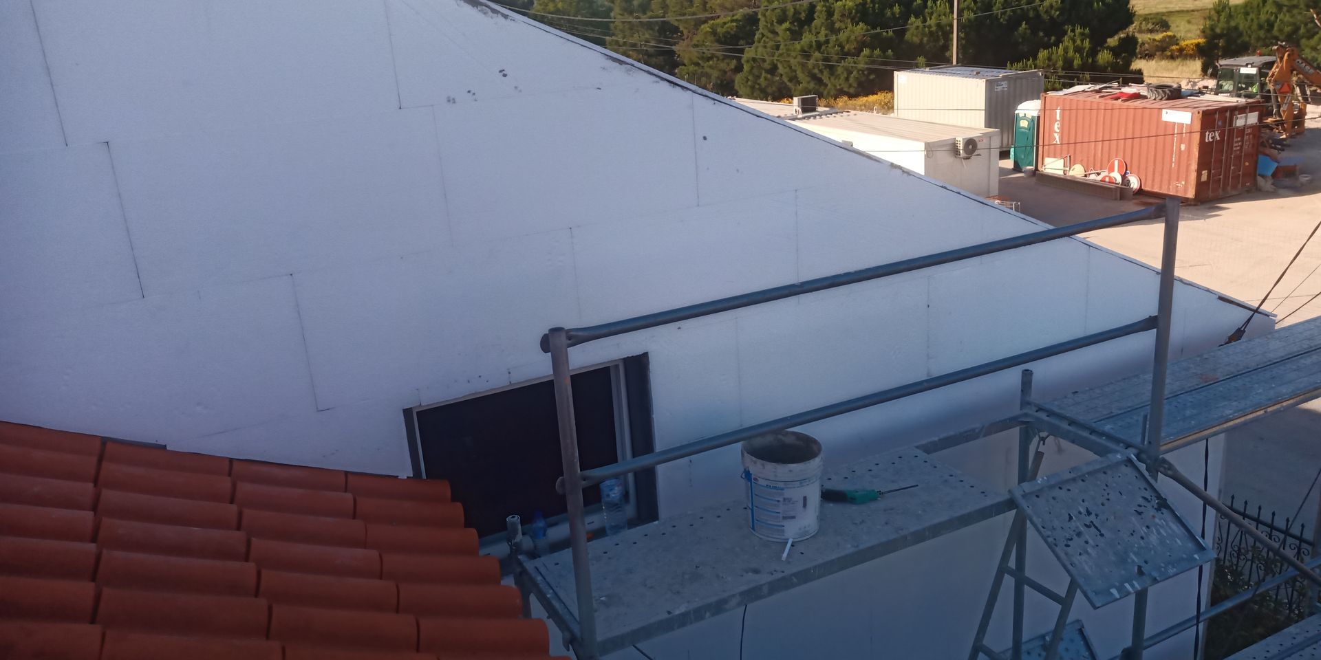 Prédio branco em obras; andaimes e telhado de telhas vermelhas à vista.