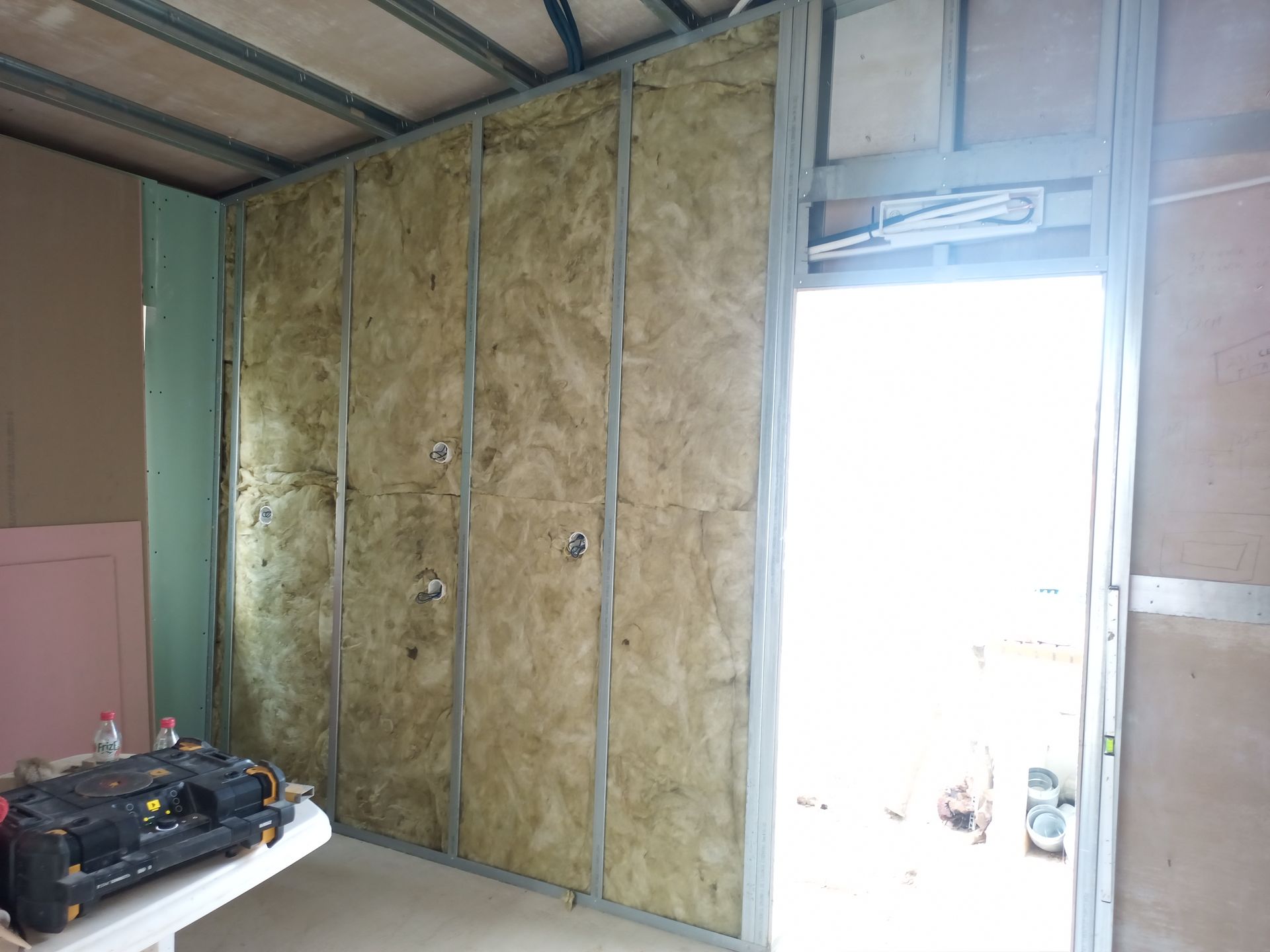 Parede interna em construção; isolamento instalado entre os perfis metálicos. Porta à direita.