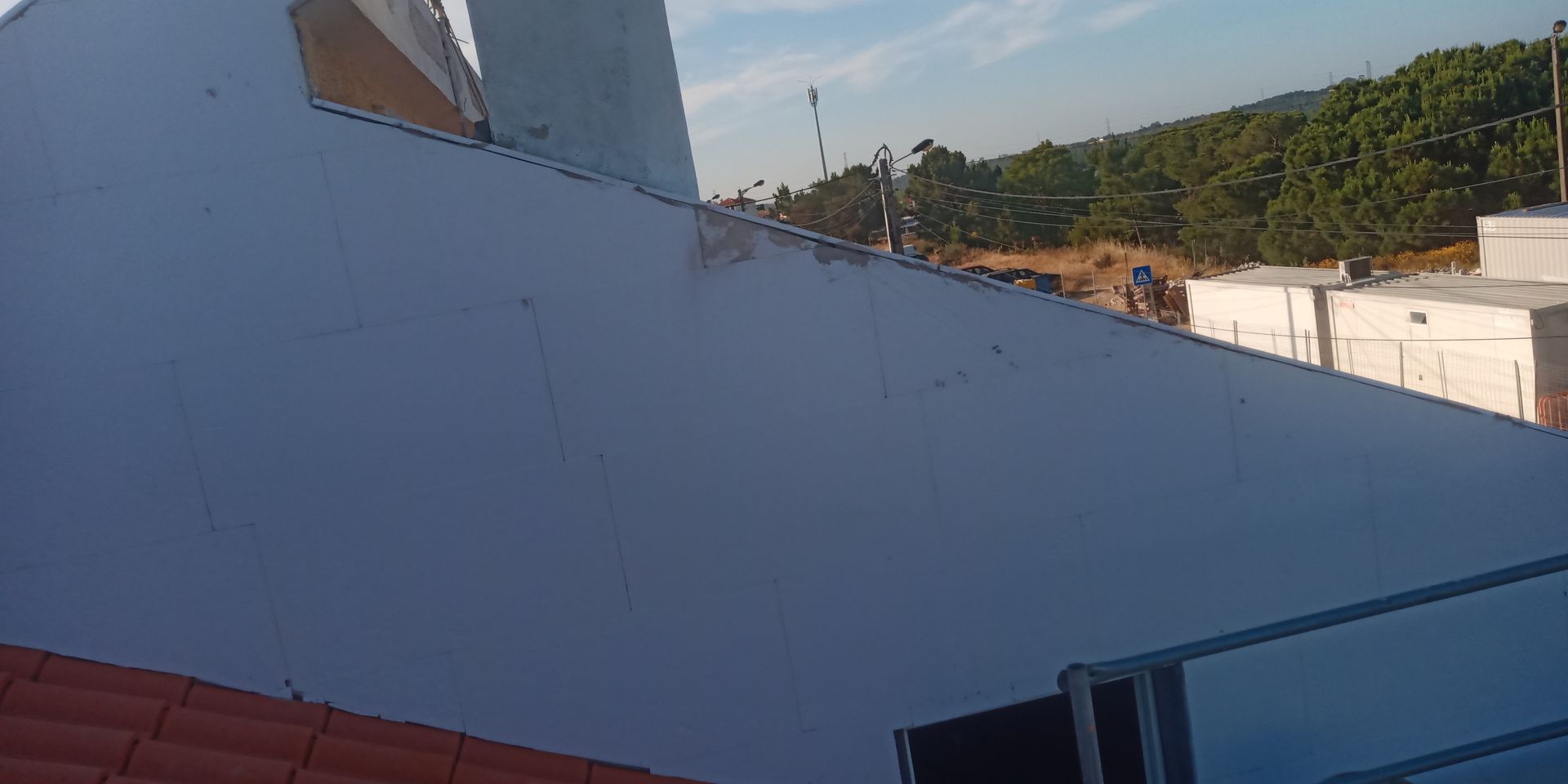 Um terraço com uma parede branca, telhas laranja e árvores ao fundo.