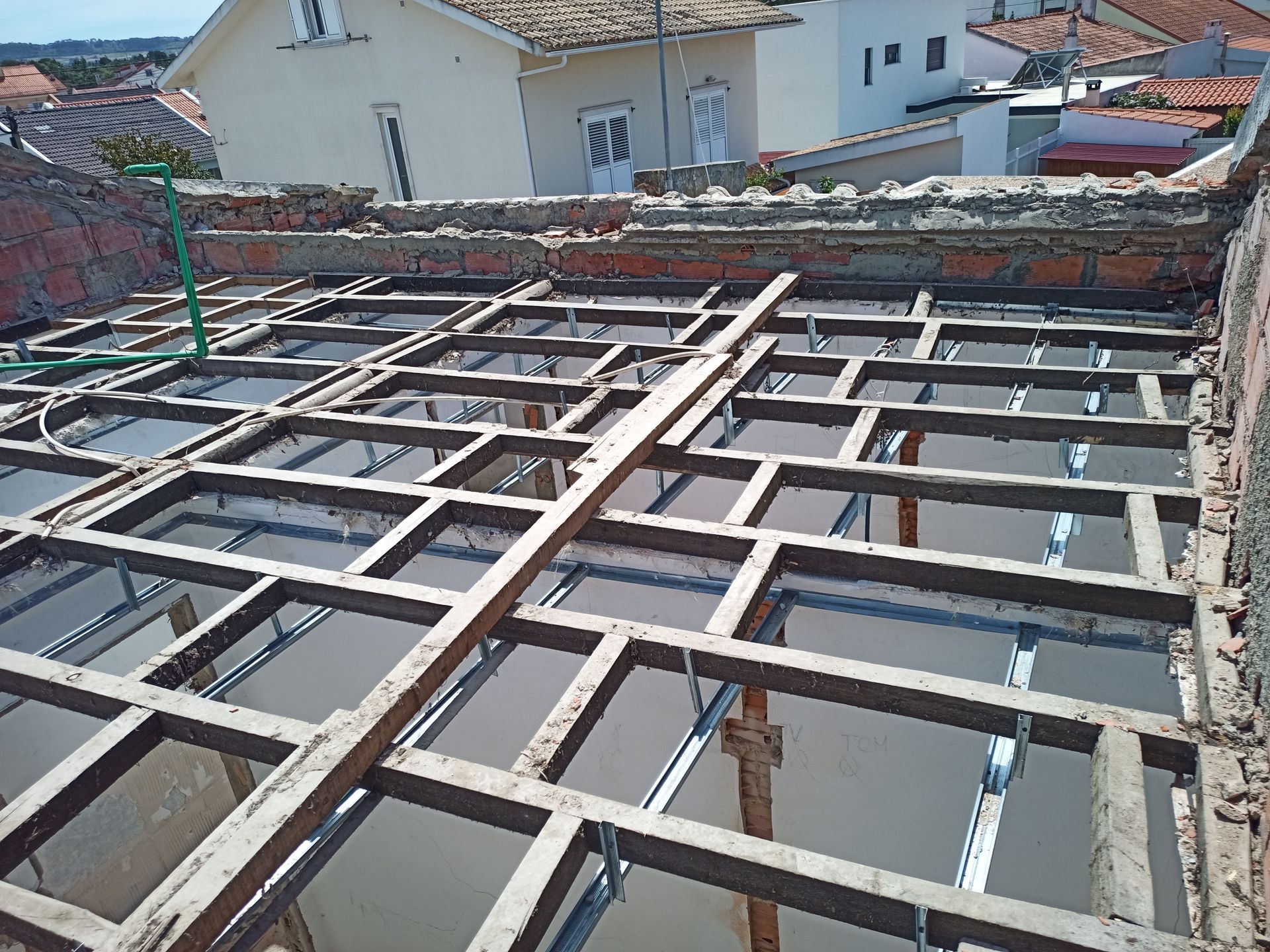 Construção de telhado: estrutura de madeira assentada sobre suportes metálicos, preparação para um novo telhado, dia ensolarado.