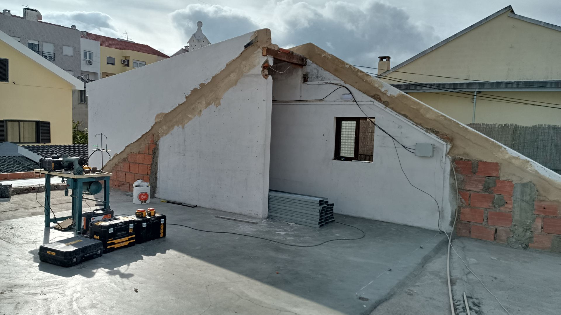 Robô próximo a um prédio branco parcialmente construído, com detalhes em tijolo e uma pequena janela.