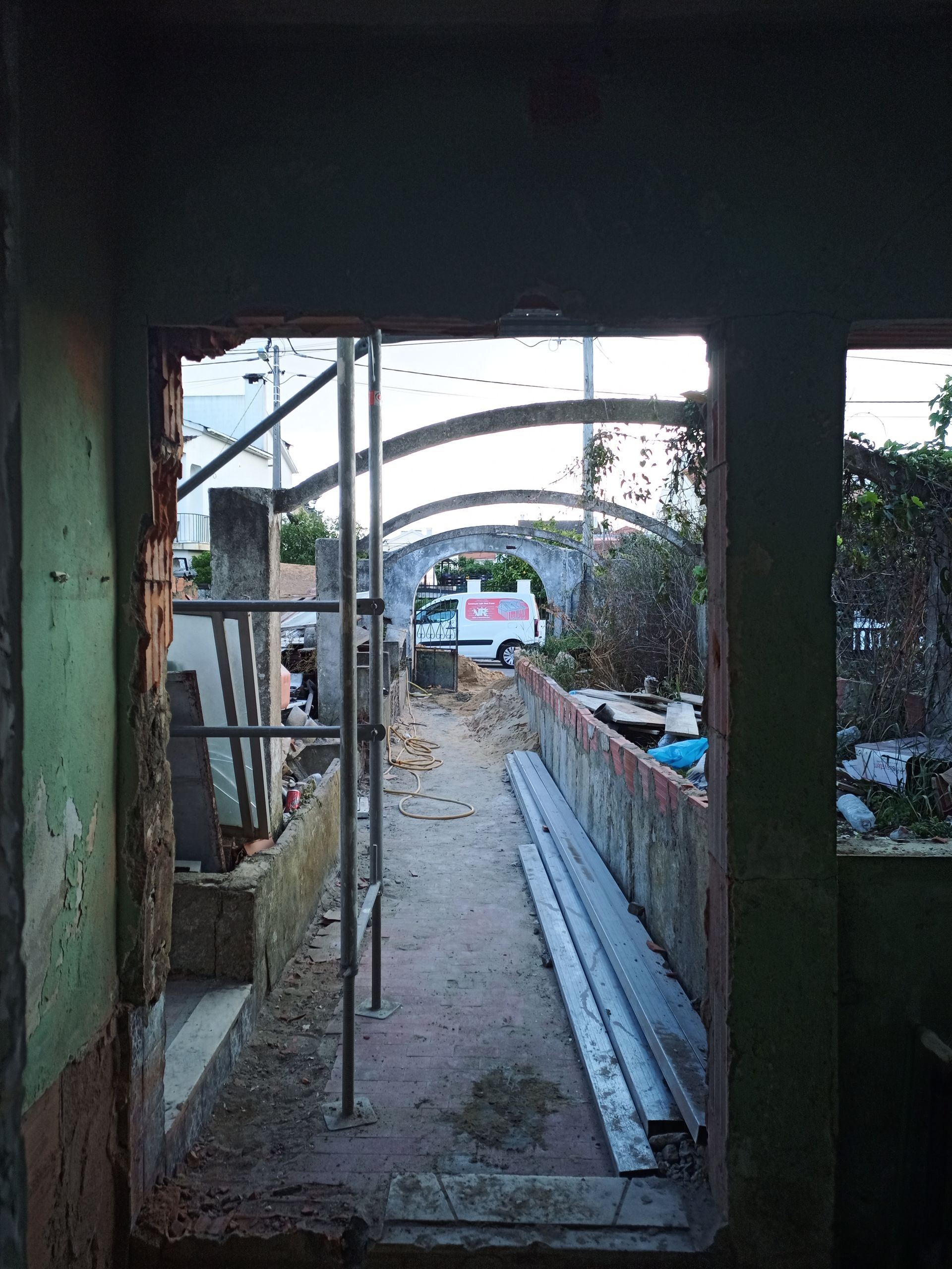 Vista através de uma porta para um canteiro de obras com uma escada, um caminhão e uma estrutura em arco.