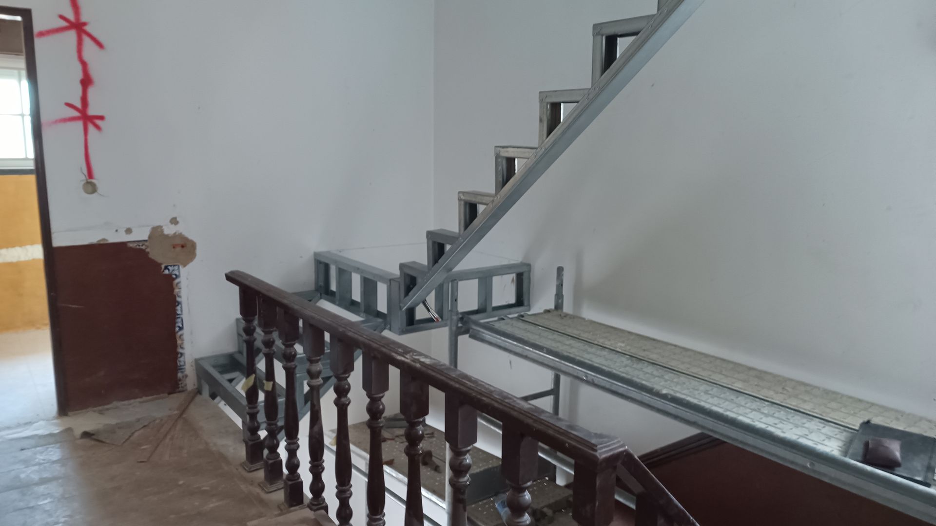 Estrutura metálica de escada em construção com corrimão de madeira. Vista interna.