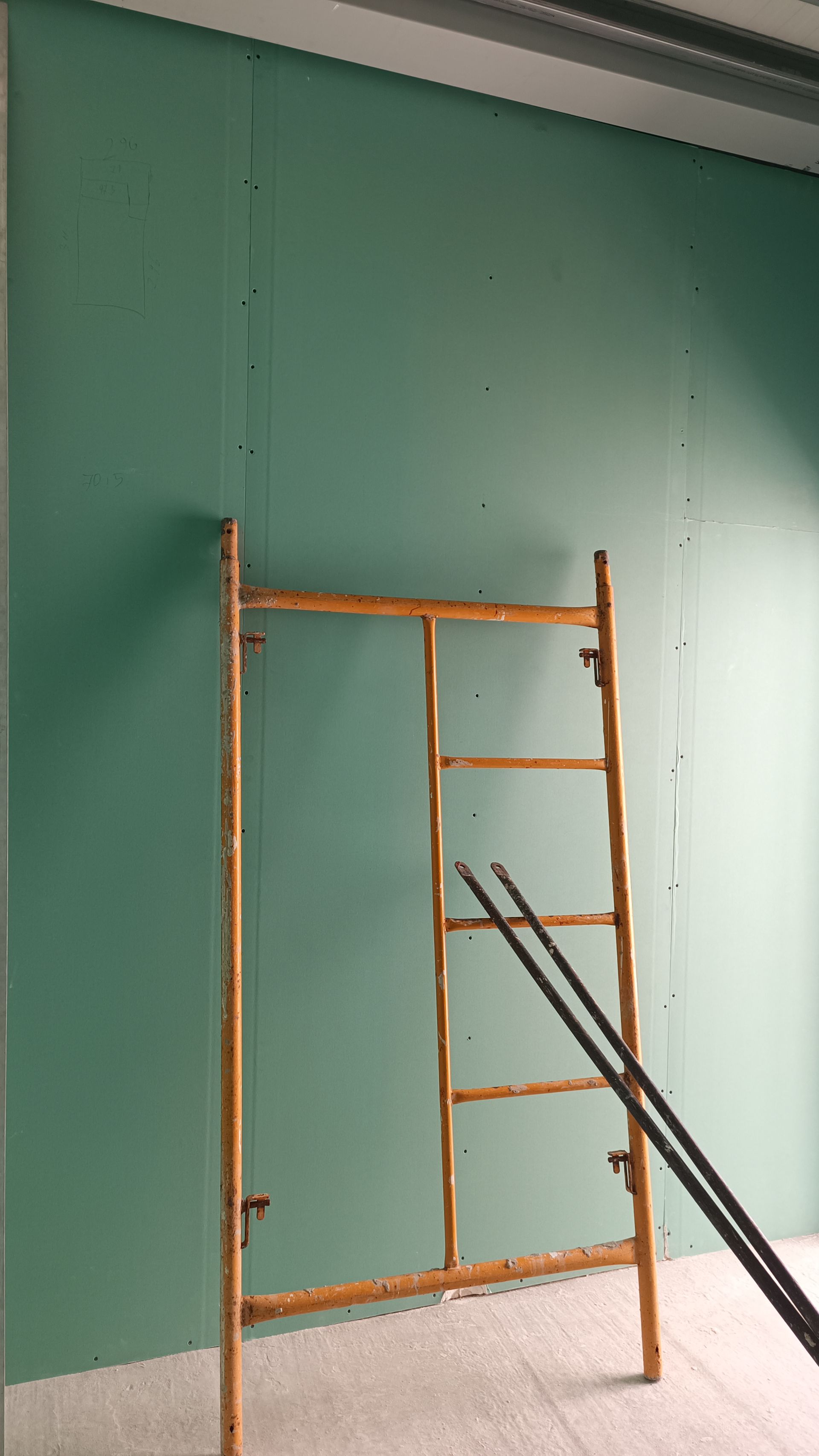 Um andaime de metal marrom está encostado em uma parede verde, com dois postes pretos próximos.