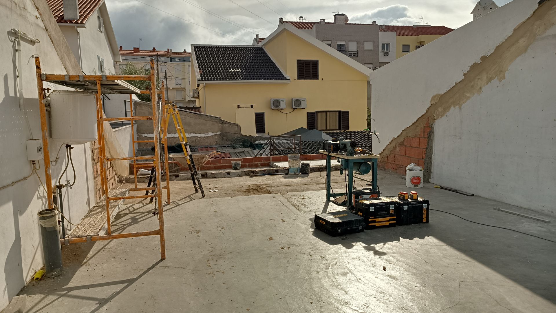 Canteiro de obras: uma pequena empilhadeira, andaimes e várias construções. Dia claro e nublado.