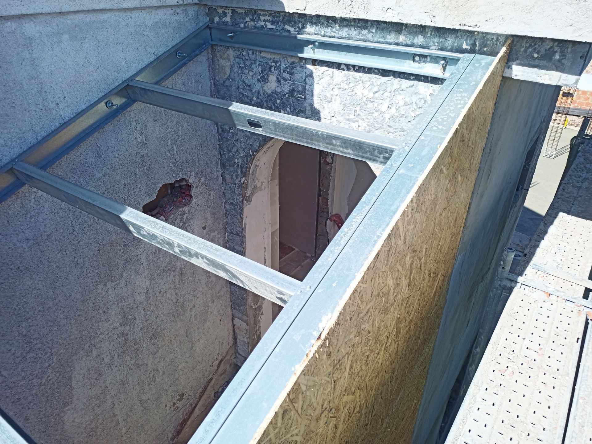 Estrutura metálica instalada em uma abertura na parede, provavelmente para uma porta ou janela. A luz do sol ilumina o interior empoeirado.