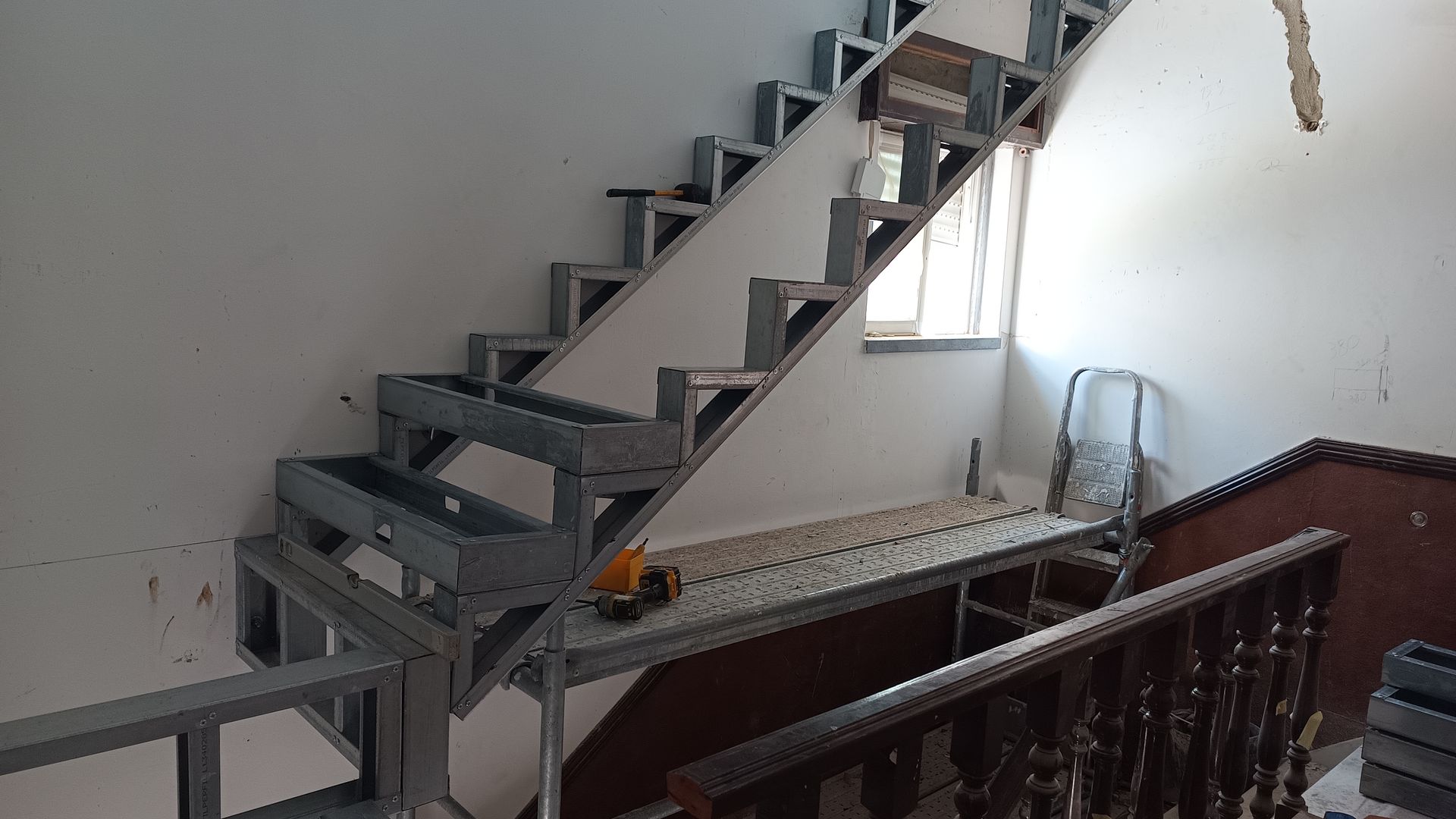 Escada com estrutura metálica em construção, adjacente a uma parede e janela.