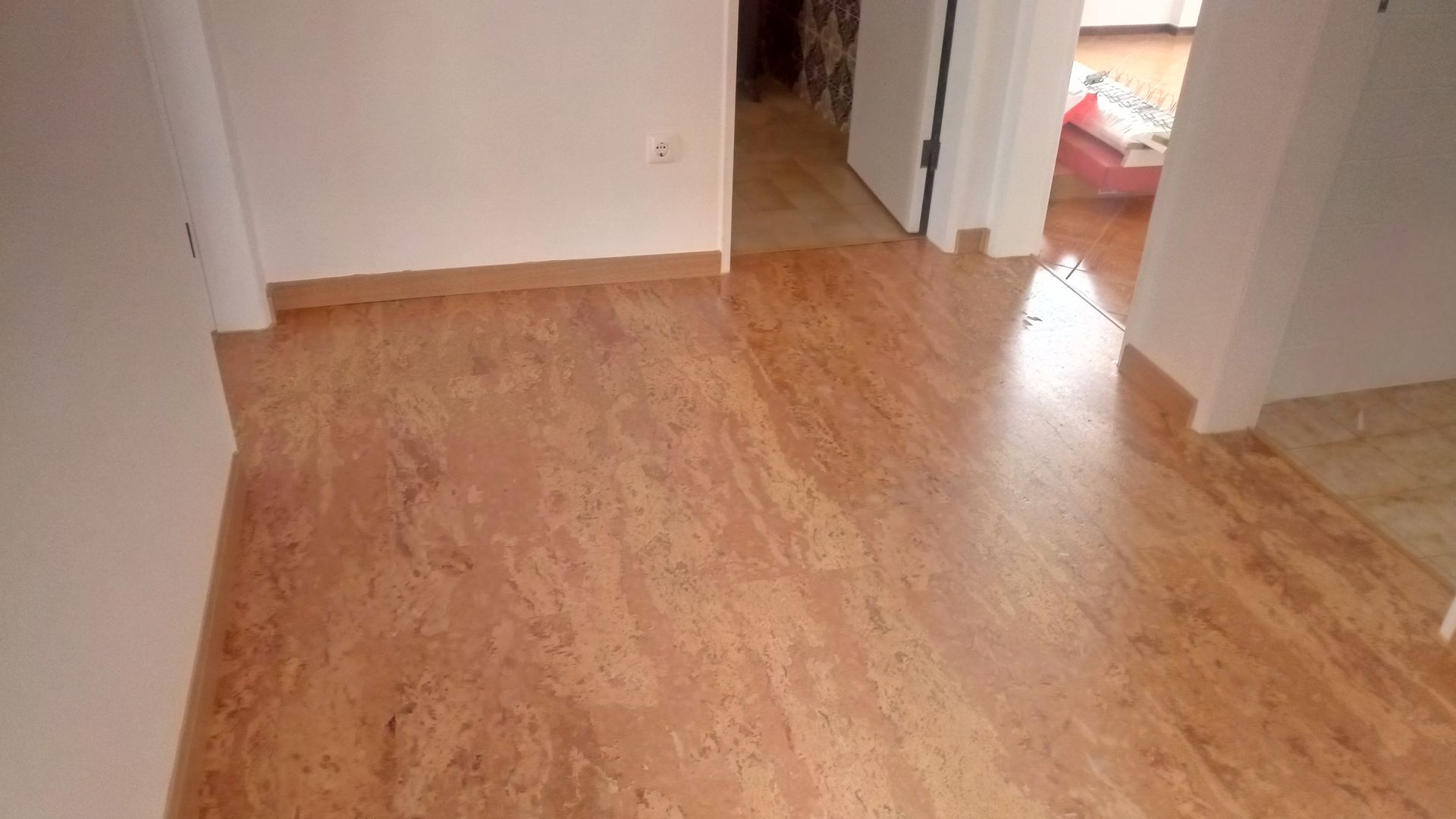 Piso de cortiça no corredor com paredes e porta brancas.