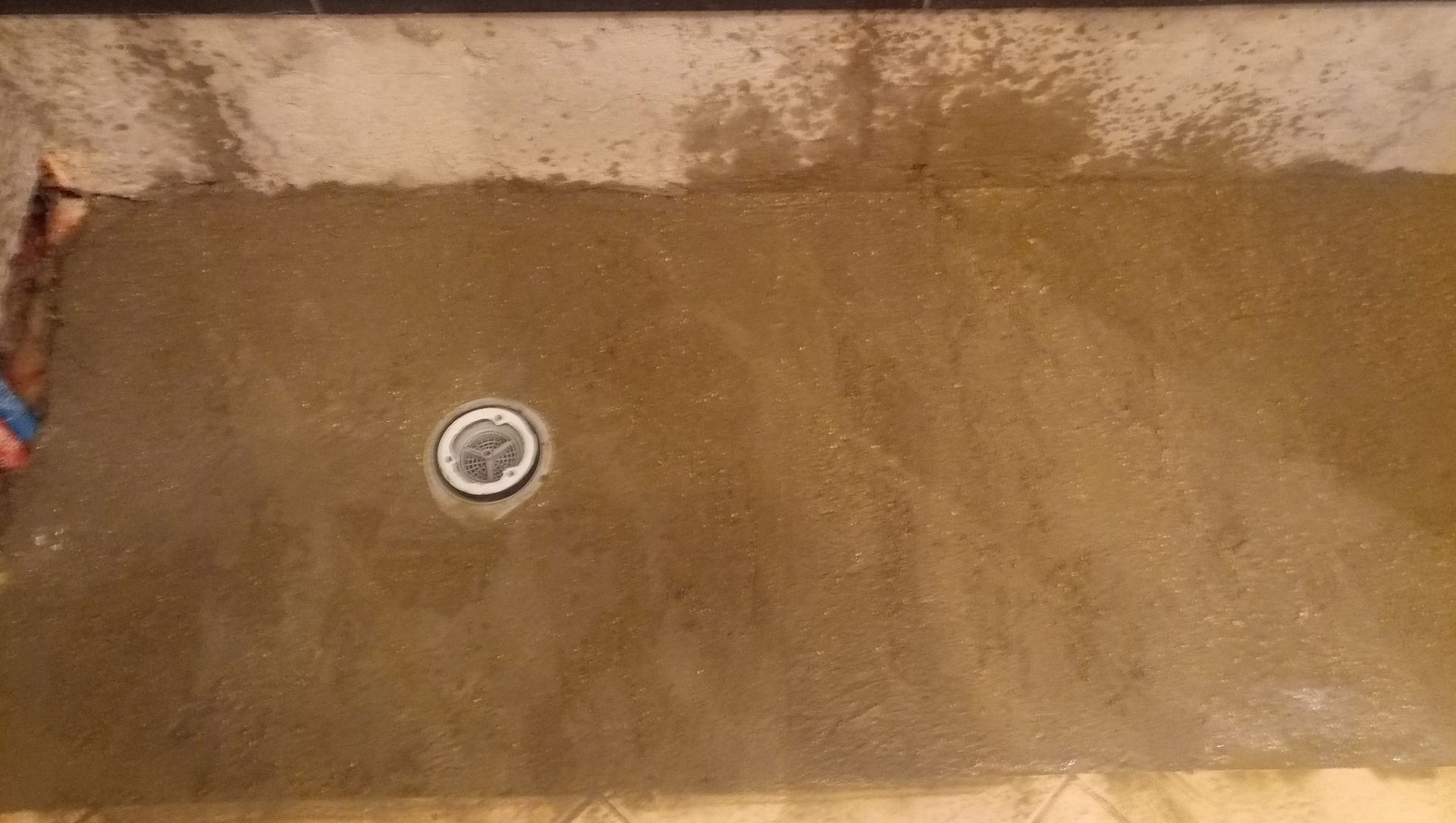 Piso de concreto molhado com um ralo no centro. Cor marrom claro.