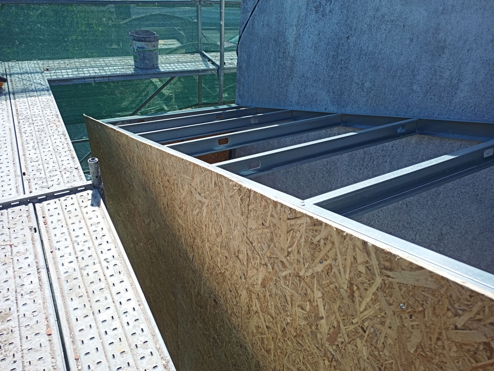 Construção em painéis de madeira com estrutura metálica, vista de um andaime em um canteiro de obras.