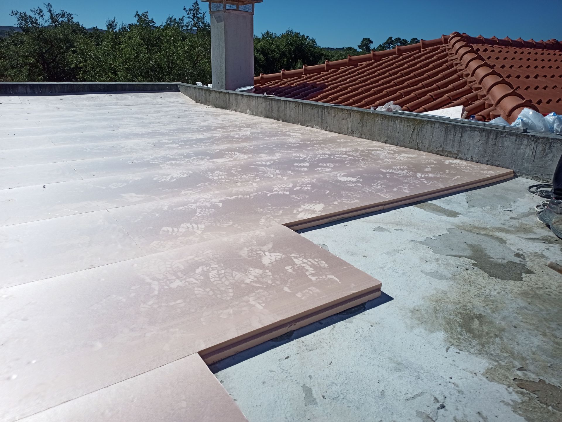 Placas de isolamento rosa instaladas sobre um telhado plano de concreto, próximo a uma chaminé e telhas.