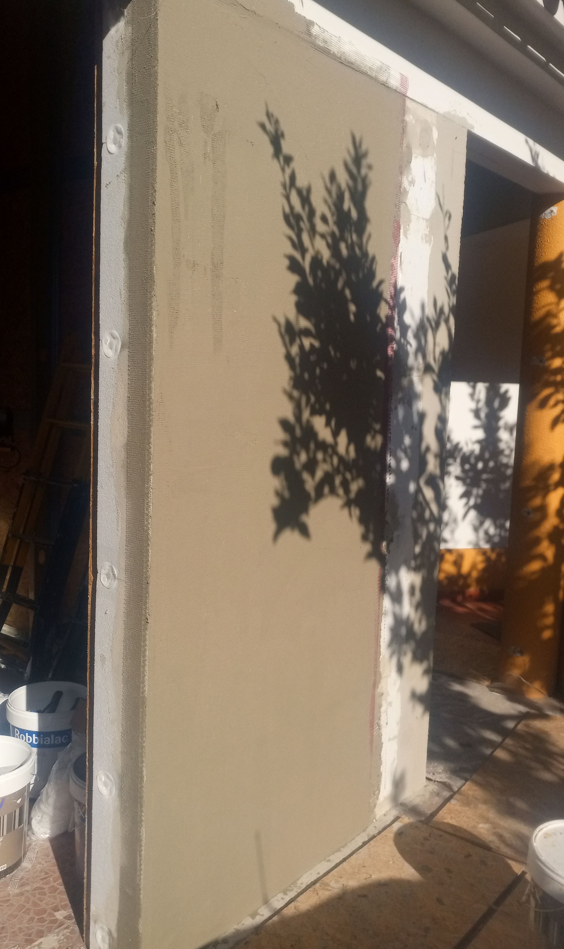 Uma parede rebocada sob a luz do sol, com a sombra de uma árvore projetada sobre ela.