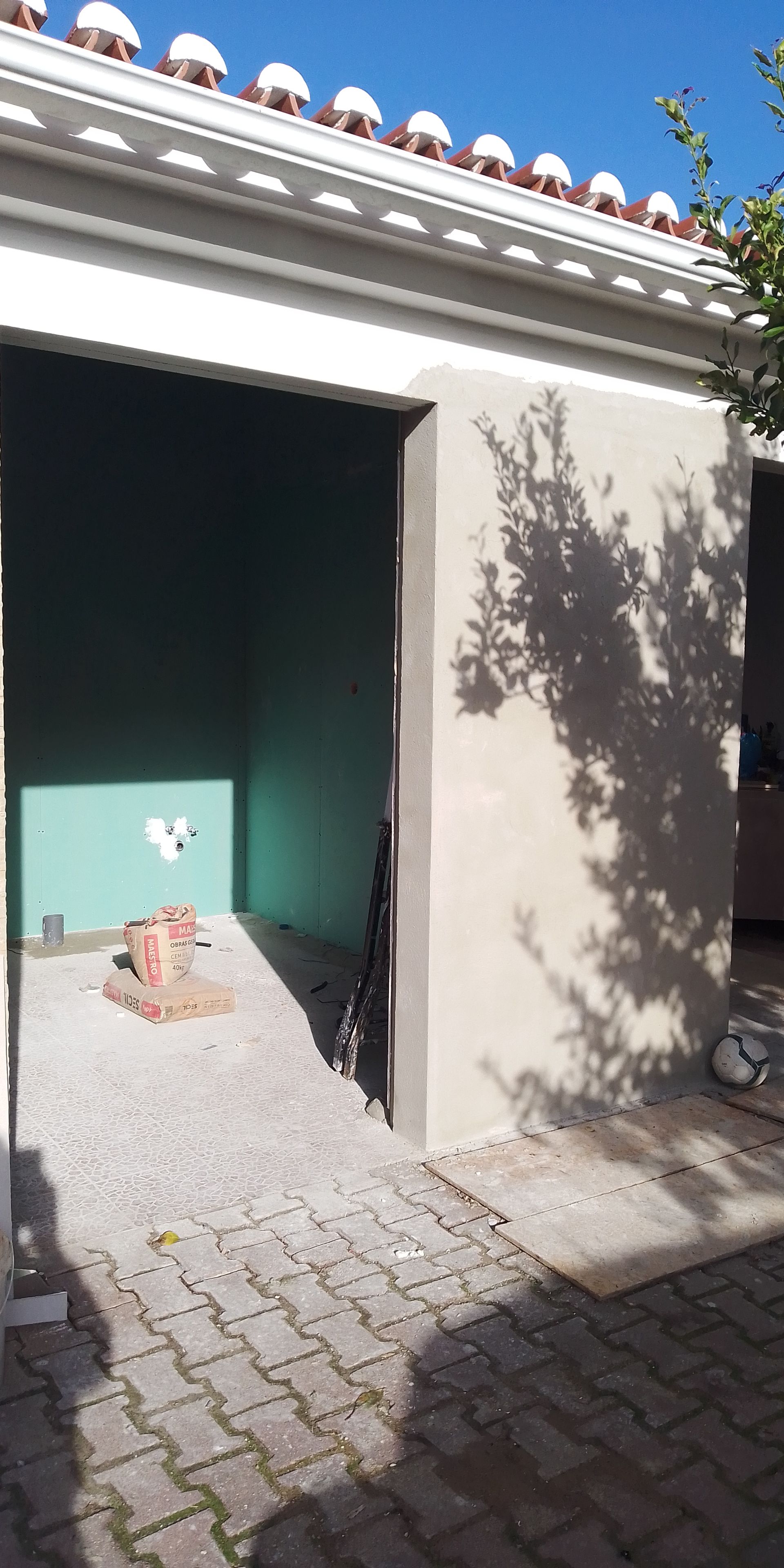 Entrada de uma estrutura com rampa e paredes internas verdes. Sombra de árvore na parede externa.