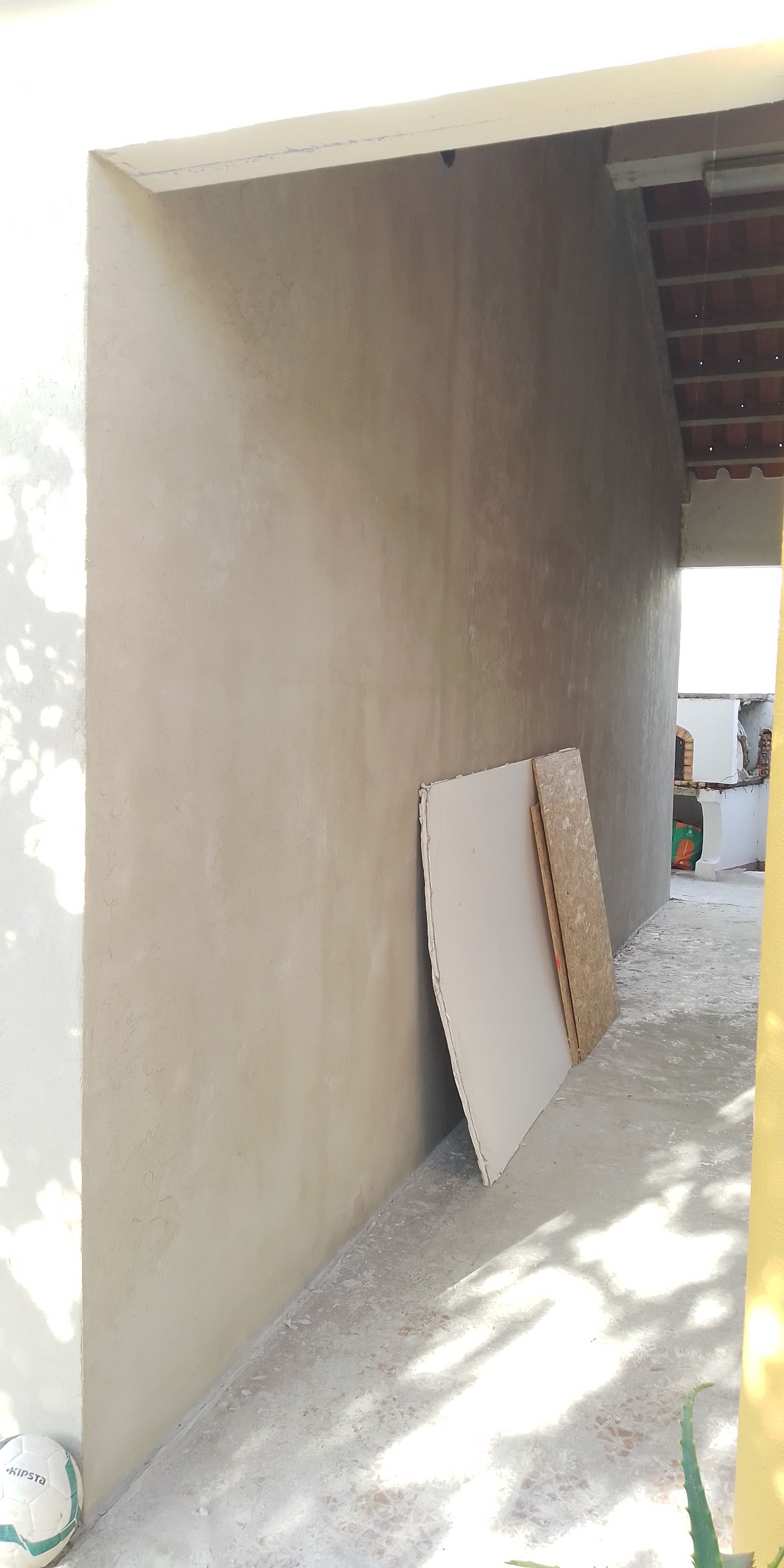 Uma parede de cor clara, com materiais de construção encostados nela, está localizada em uma entrada.