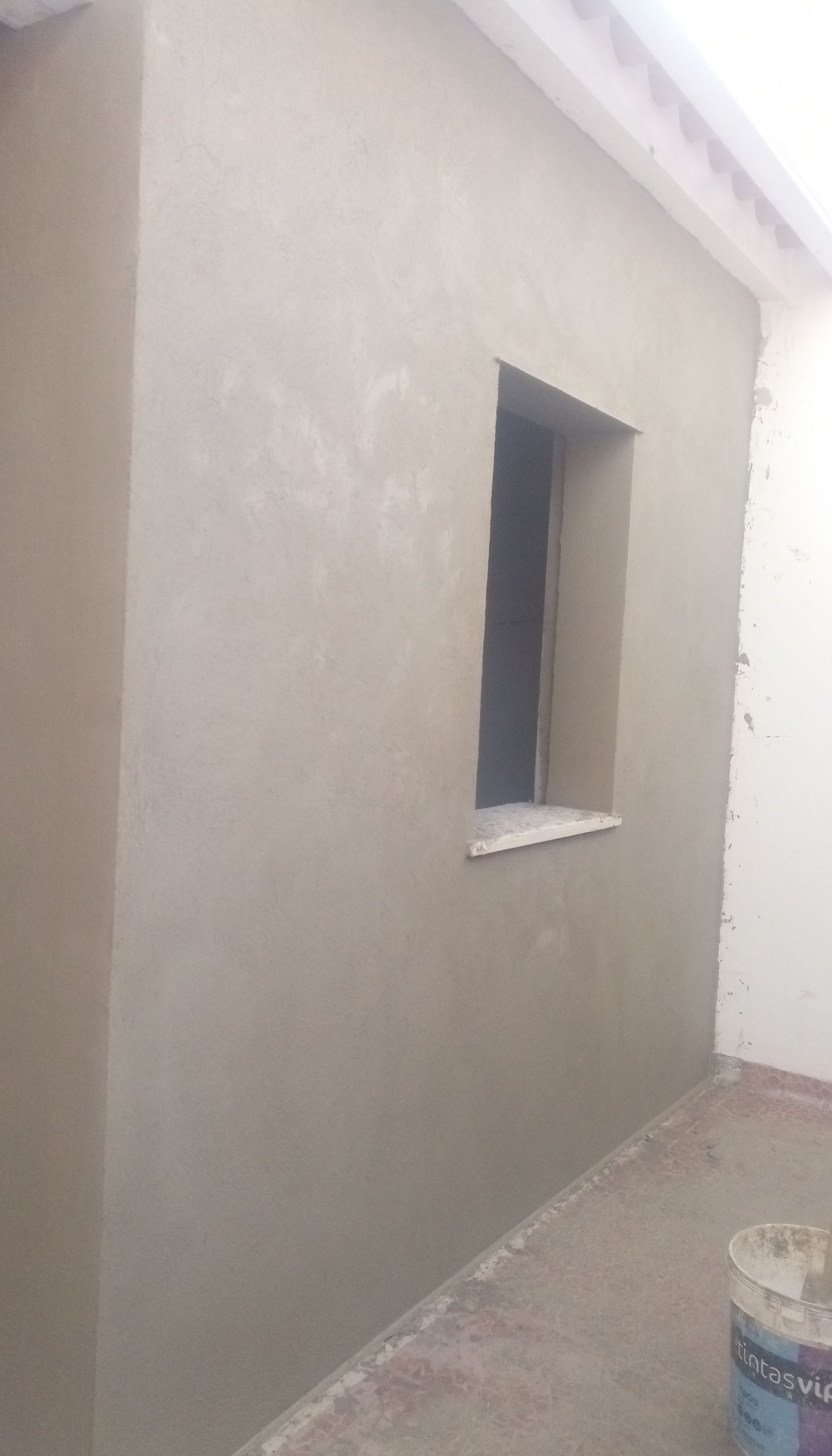 Parede externa com janela quadrada, revestida com estuque fresco.