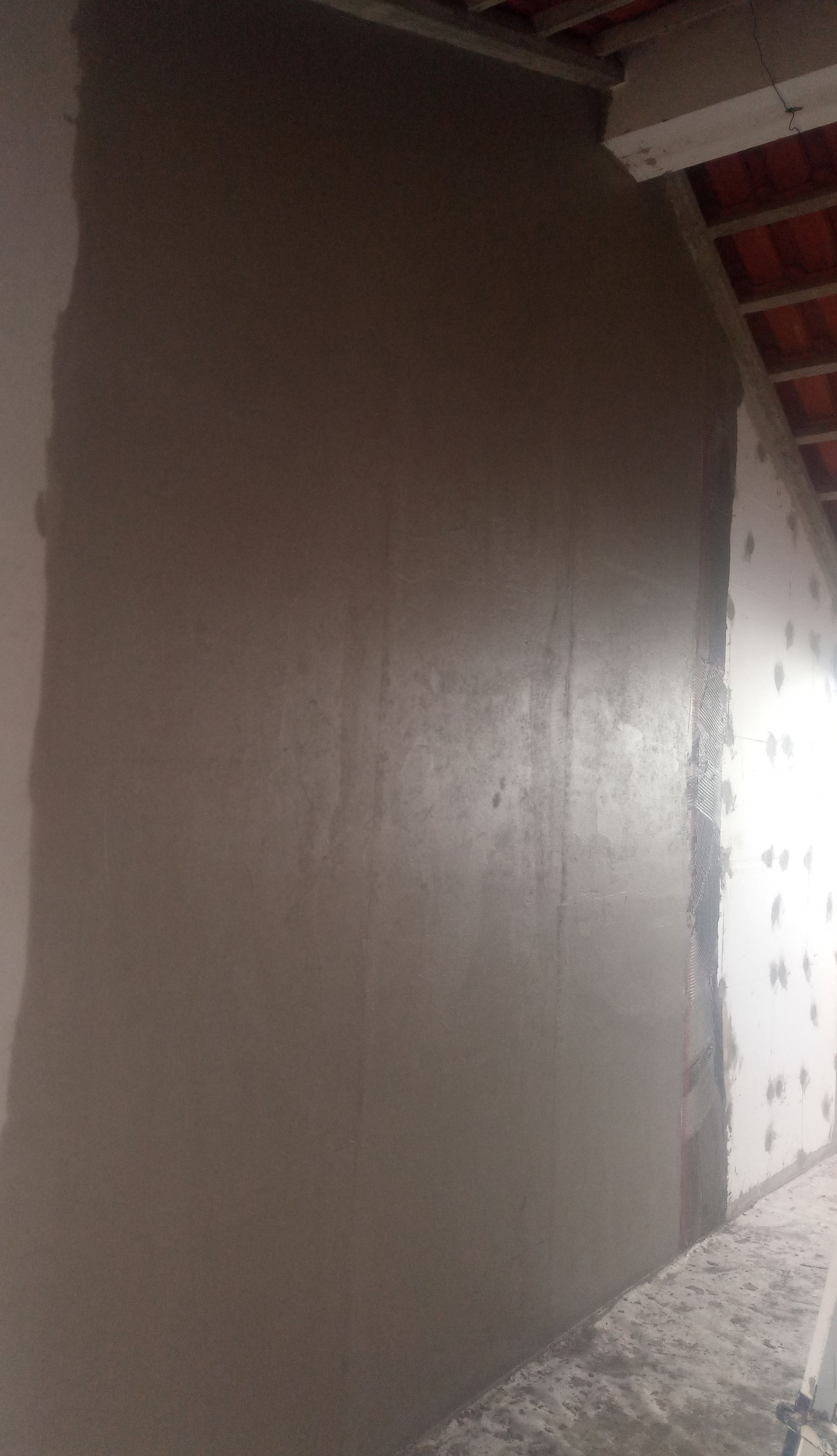 Parede rebocada de cinza em construção; parcialmente acabada, com marcas verticais visíveis da desempenadeira.