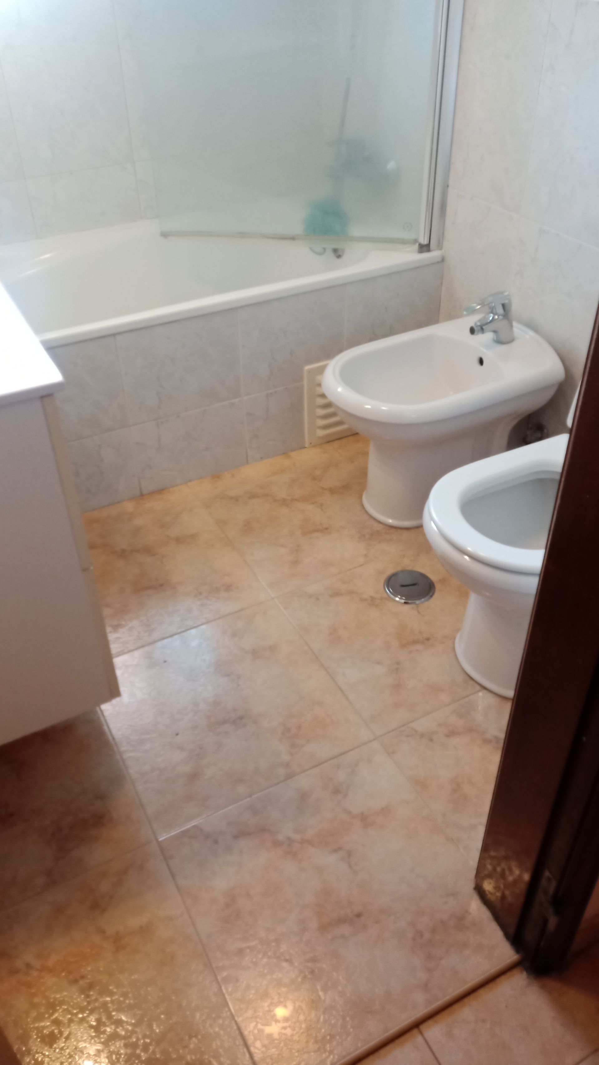 Banheiro com banheira, bidê e vaso sanitário. Piso de azulejo bege e louças sanitárias brancas.