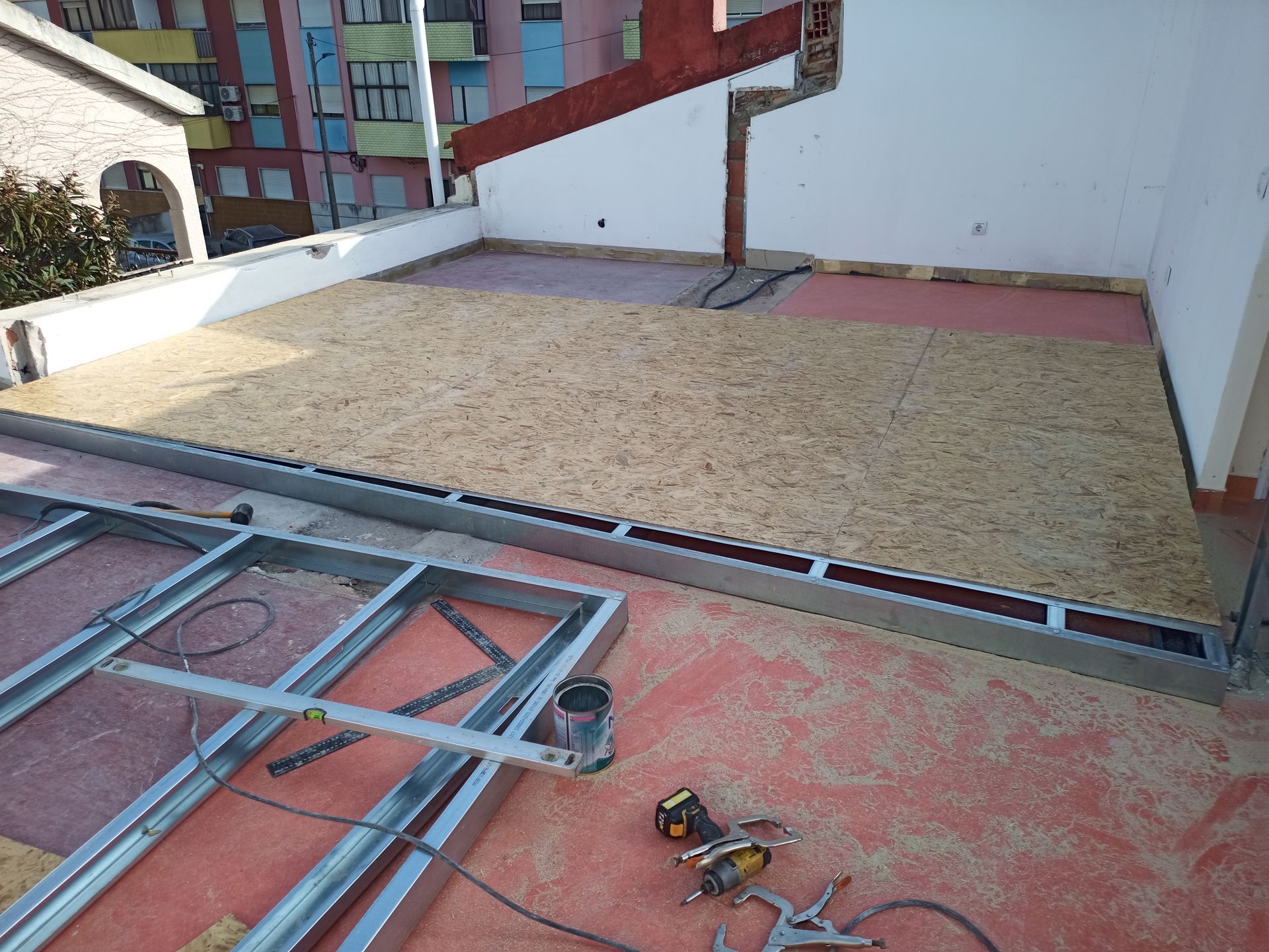 Construção de um telhado plano com estrutura metálica, tábuas de madeira e ferramentas, ao ar livre, no último andar de um edifício.