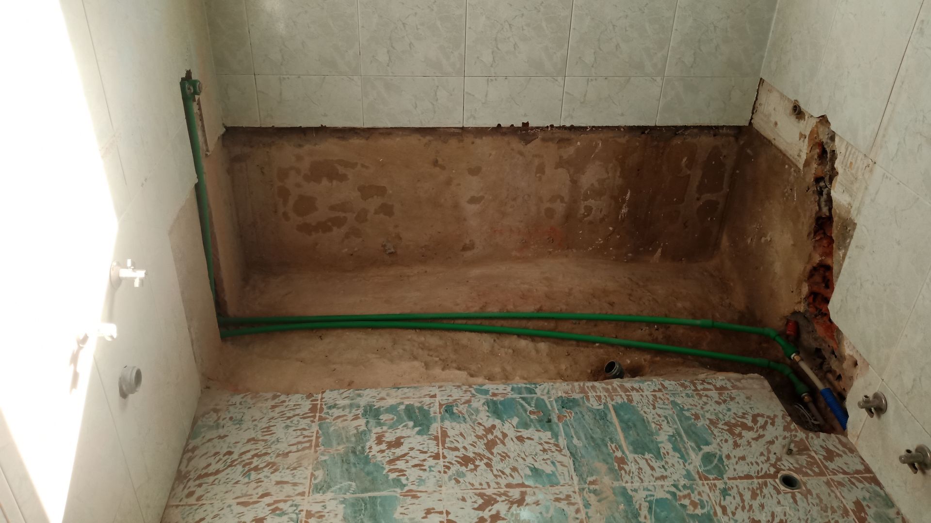 Banheiro em reforma com encanamento exposto e azulejos parcialmente removidos.