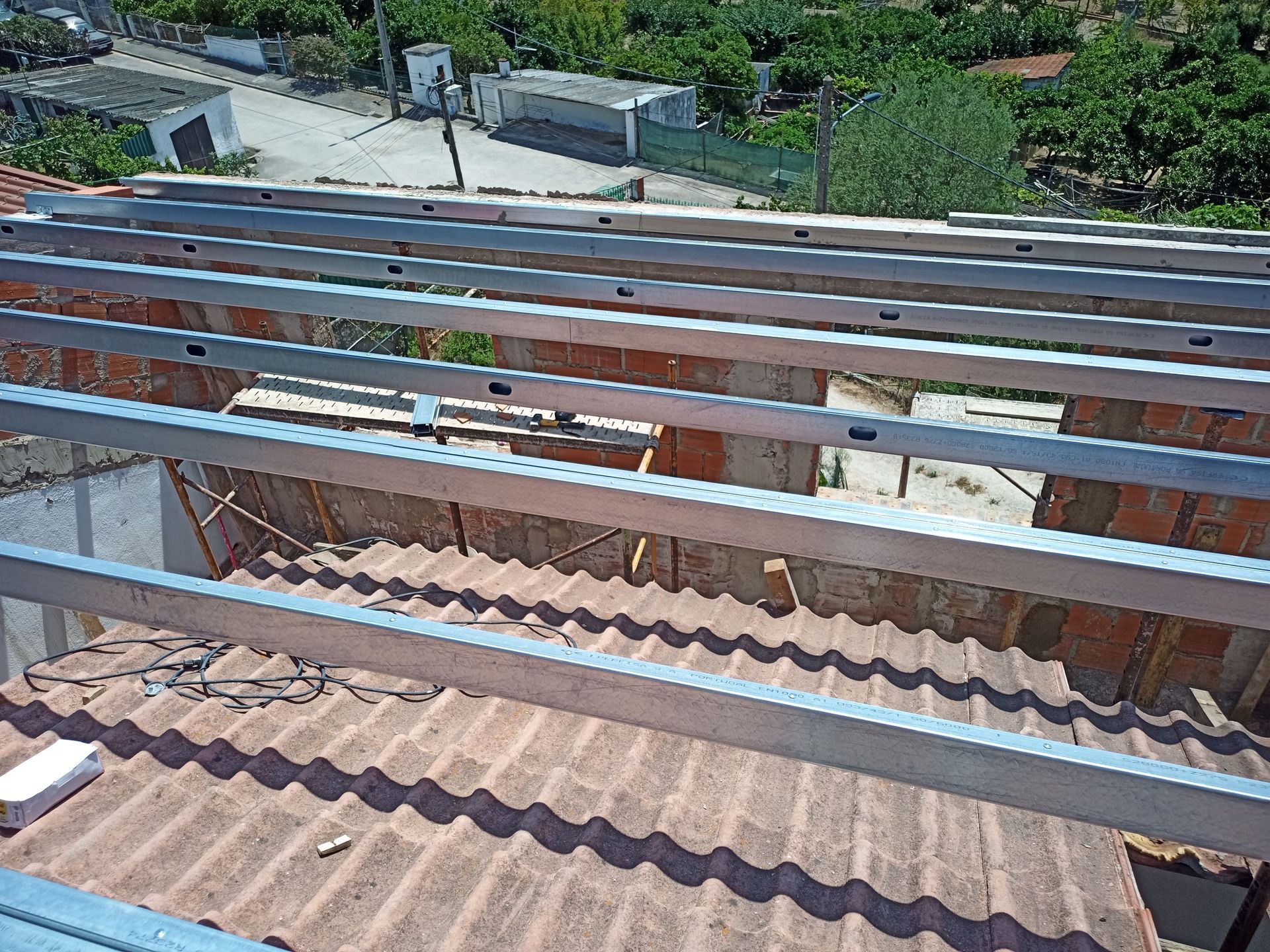 Trilhos metálicos instalados em um telhado de telhas vermelhas, preparando o local para a montagem de painéis solares.