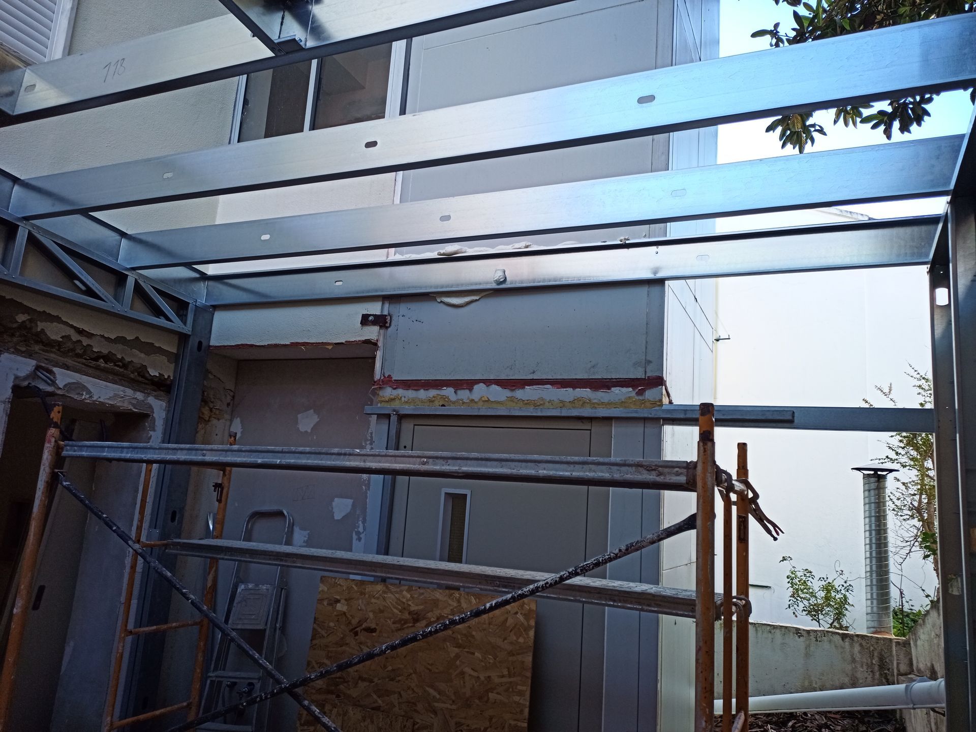 Estrutura metálica de um edifício em construção, mostrando as vigas e uma parede parcialmente acabada.