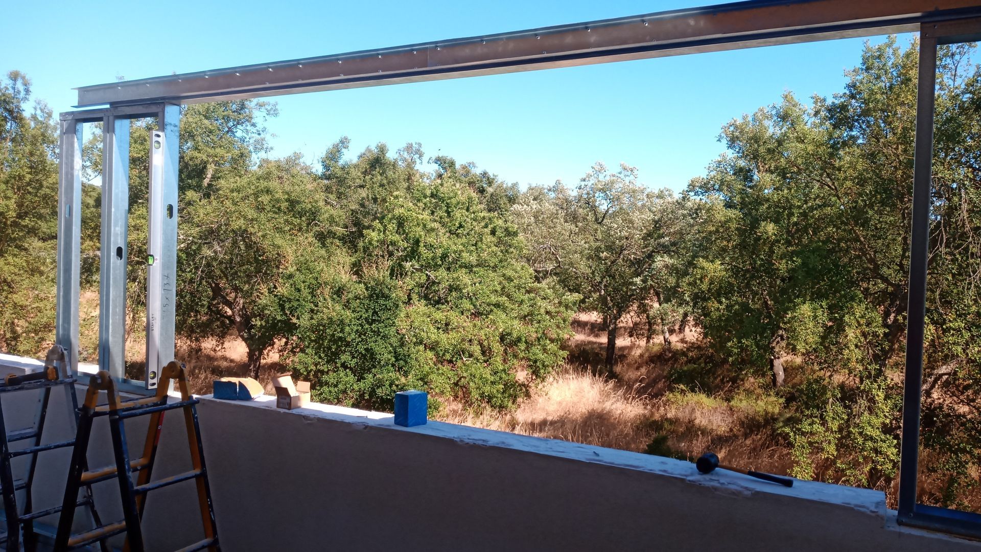 Estrutura metálica de uma construção em andamento, aberta para a vista das árvores e do céu.