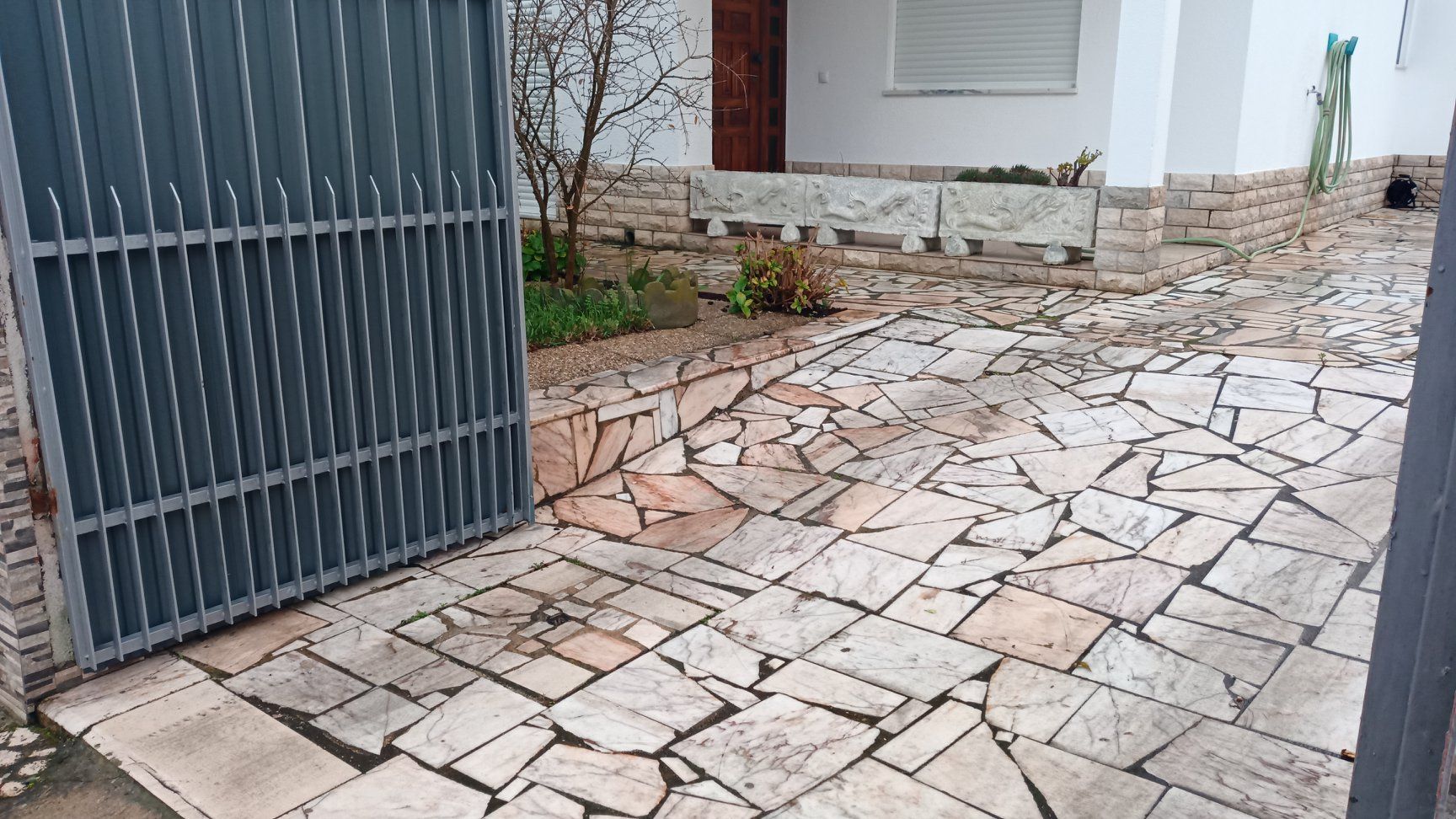 Um portão de metal cinza dá acesso a uma entrada de pedra que leva a um edifício branco.