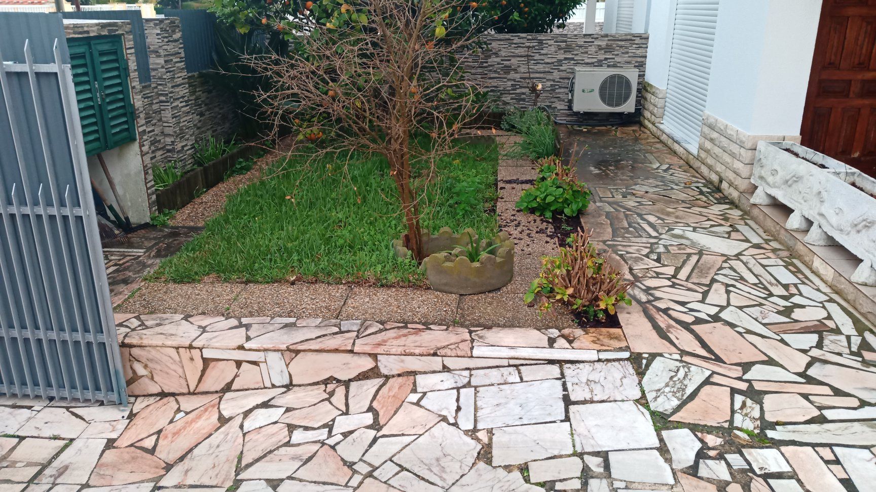 Um pequeno jardim com caminho de pedra e grama, ao lado de uma casa com portão.