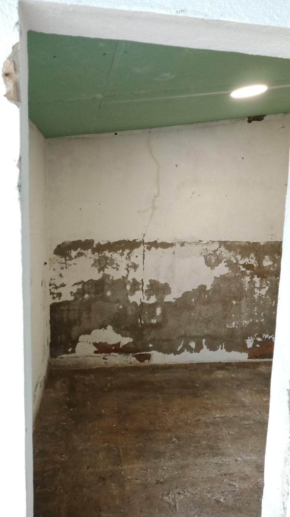 Uma pequena sala vazia com tinta descascando nas paredes e piso de concreto, vista da porta.