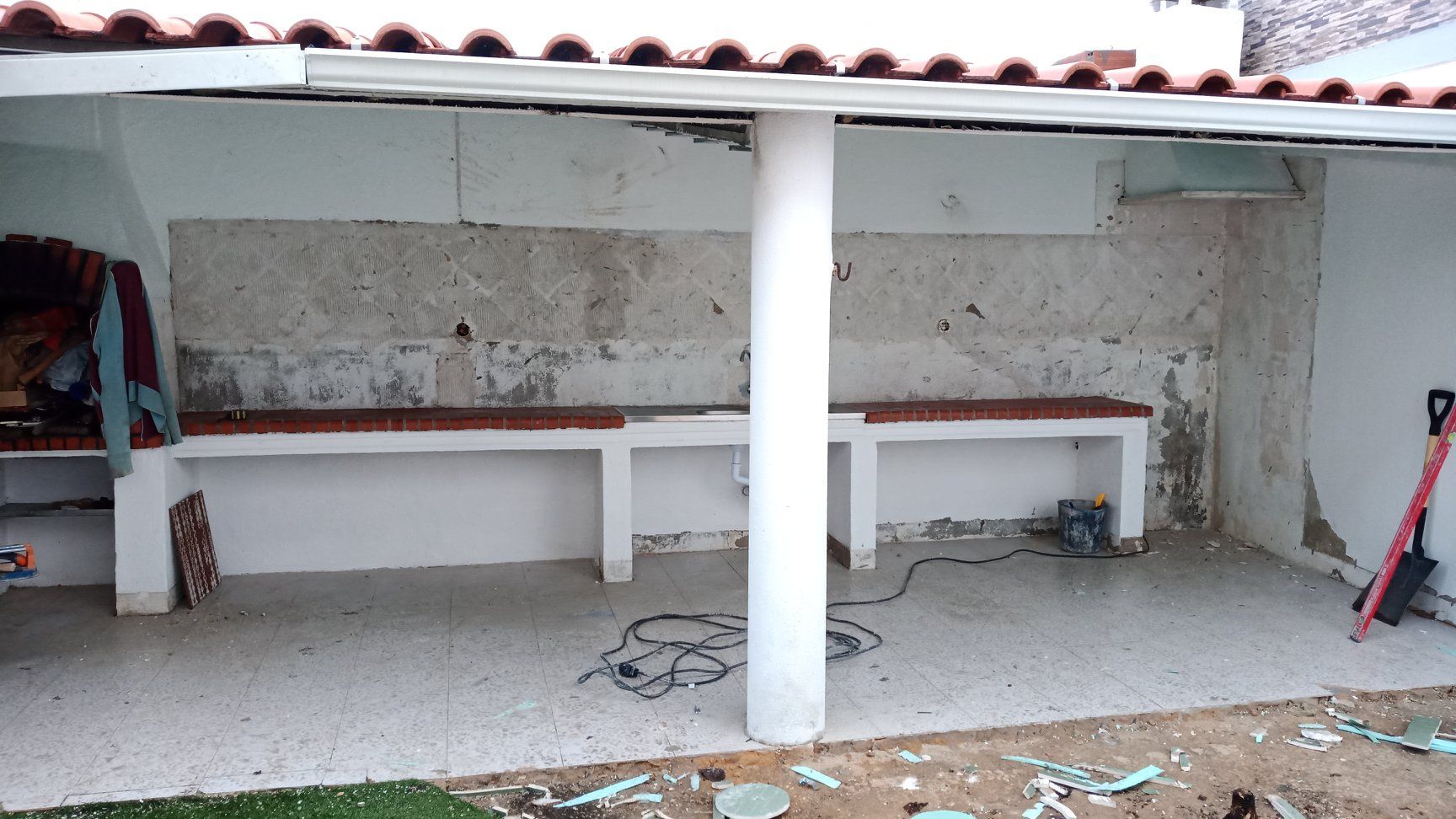 Área externa coberta com bancos embutidos, um pilar branco e uma parede texturizada.