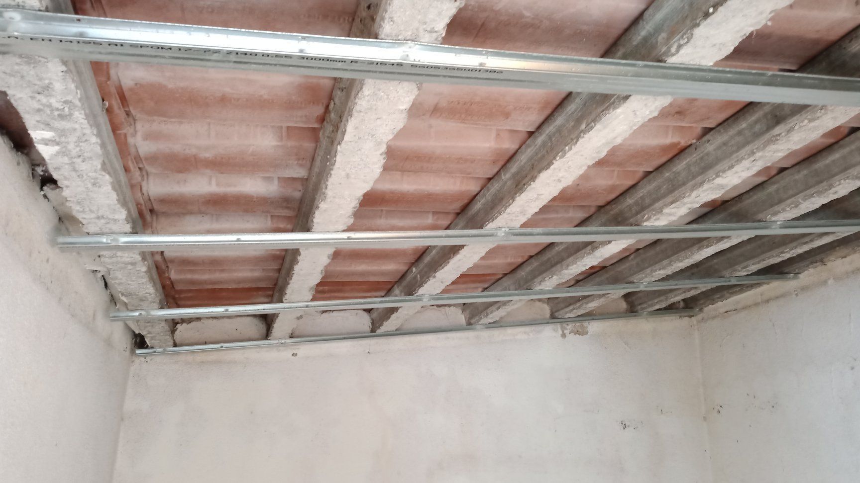 Estrutura metálica instalada em teto de tijolos, preparando-se para a instalação de drywall. Paredes bege.
