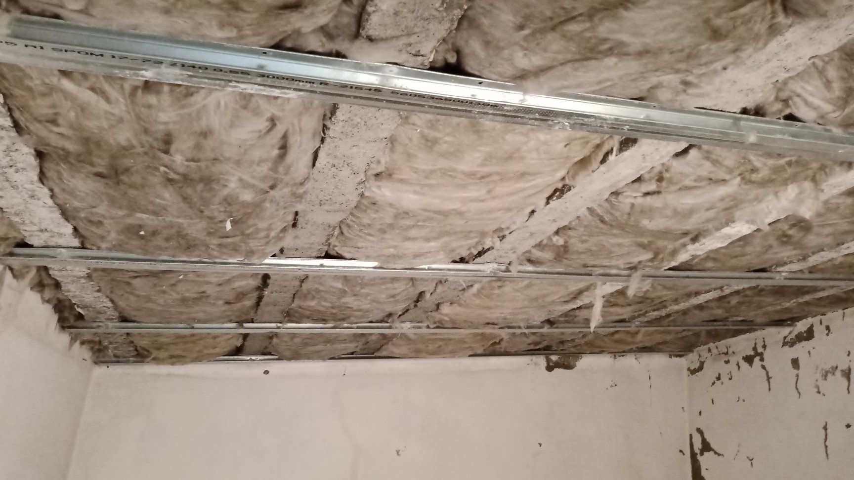 Isolamento do teto exposto, vigas de sustentação metálicas, drywall danificado, vista interna.