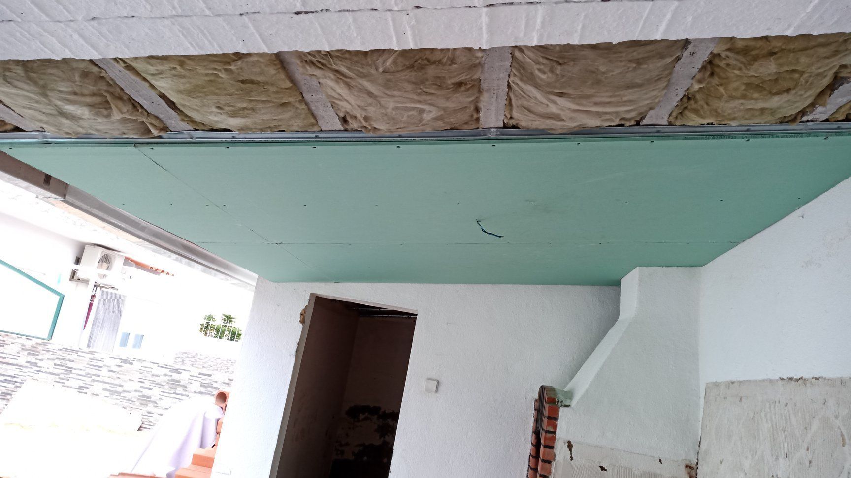 Teto em construção: drywall verde, isolamento, estrutura metálica e paredes inacabadas.