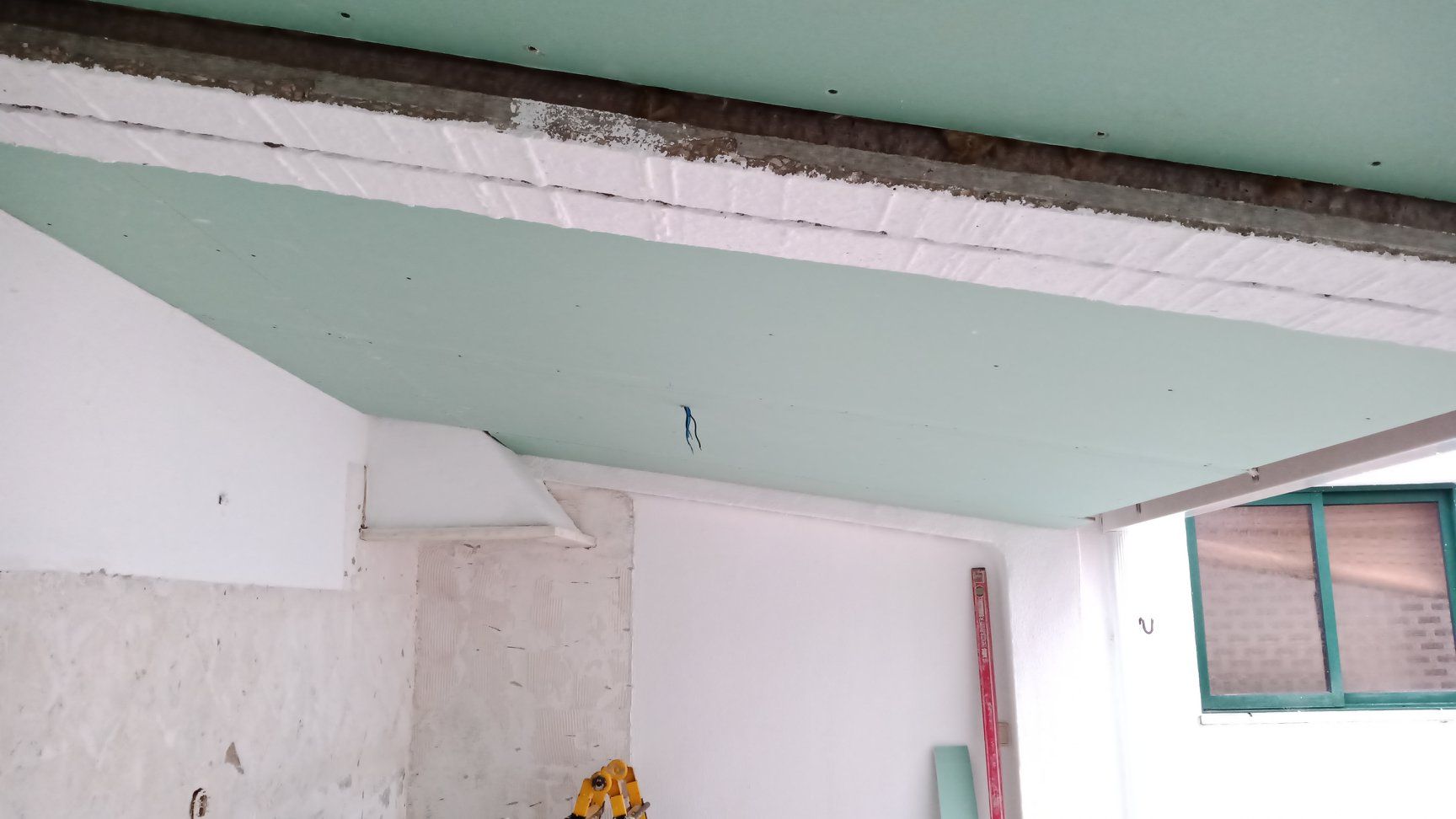 Construção interior: Teto em gesso cartonado verde, paredes brancas, vigas expostas.