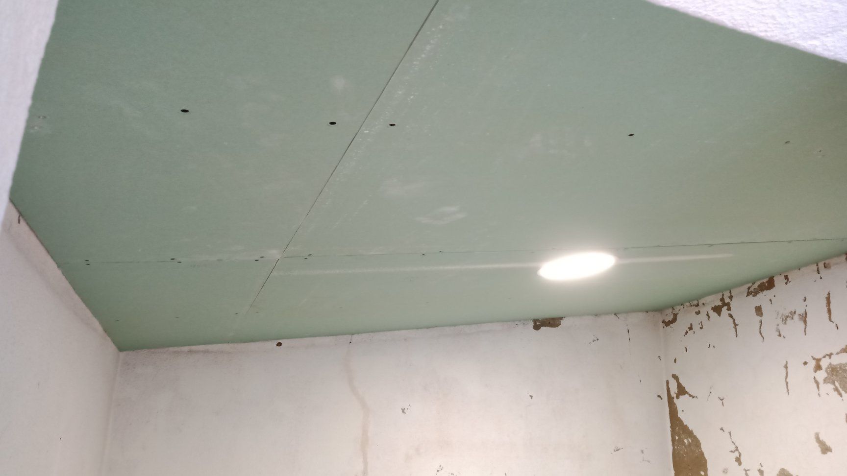 Teto de gesso cartonado verde com iluminação embutida, em uma sala com paredes brancas e gesso aparente.