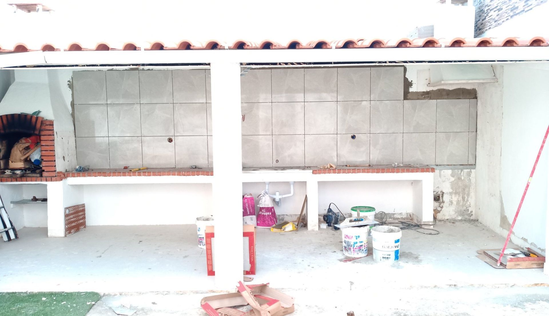 Cozinha externa em construção, com churrasqueira de tijolos, bancadas de concreto e paredes inacabadas.