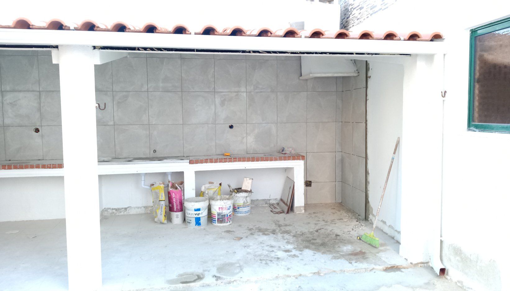 Cozinha externa em construção, com bancadas, paredes e materiais de cimento.