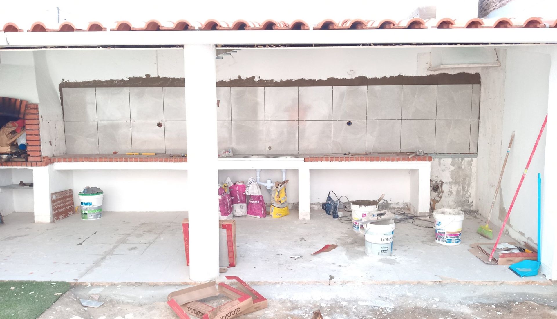Pátio externo em construção com bancadas, alvenaria e materiais de construção inacabados.