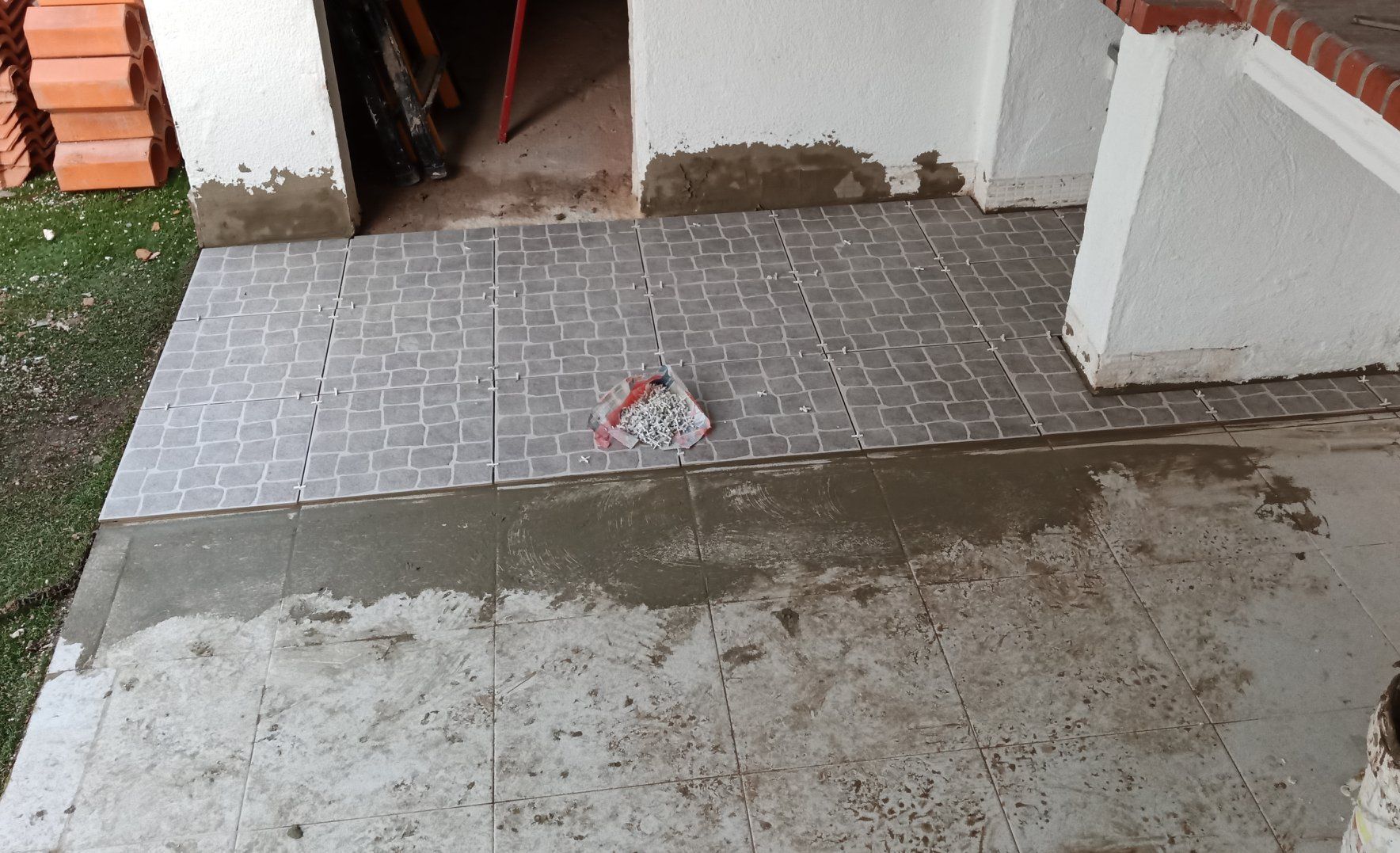 Trecho de pátio recém-azulejado com ladrilhos cinza, cimento e entulho de construção.
