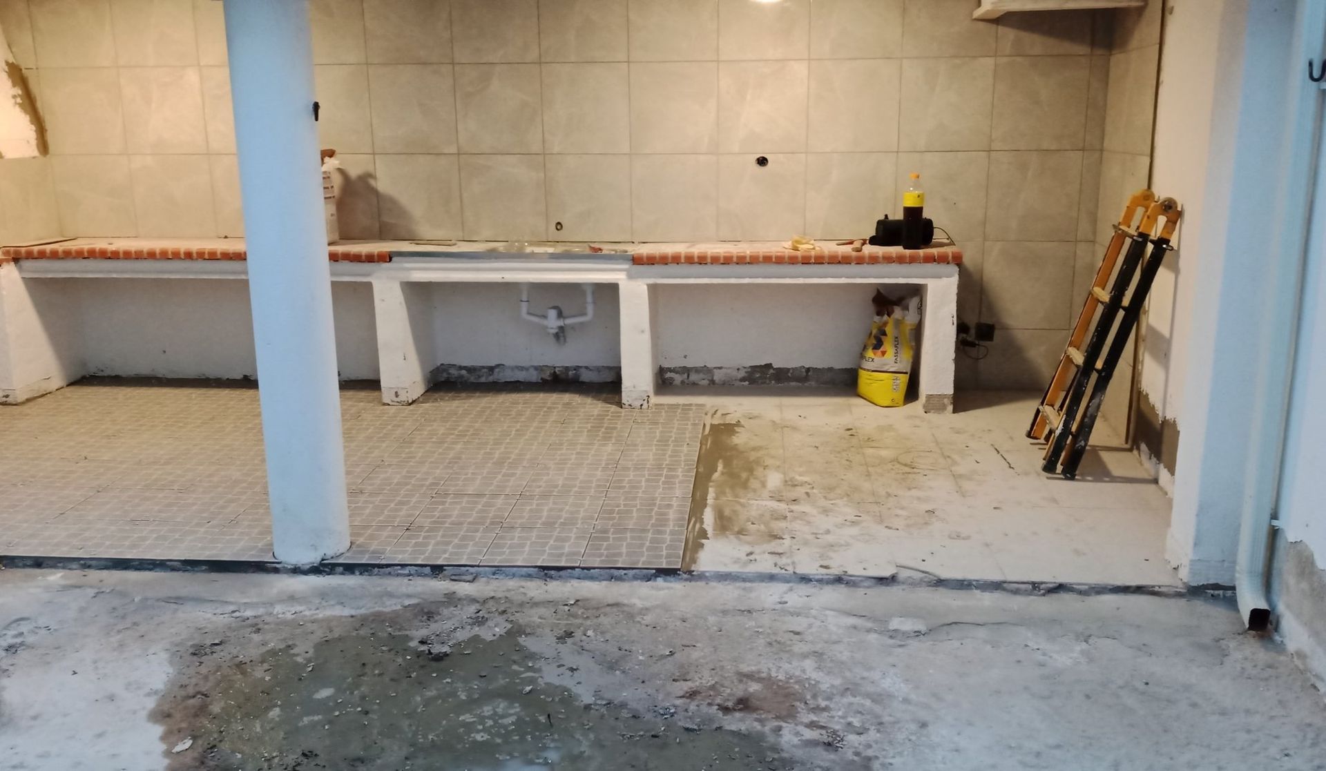 Sala de concreto em construção, com backsplash de azulejos, bancada exposta e ferramentas.