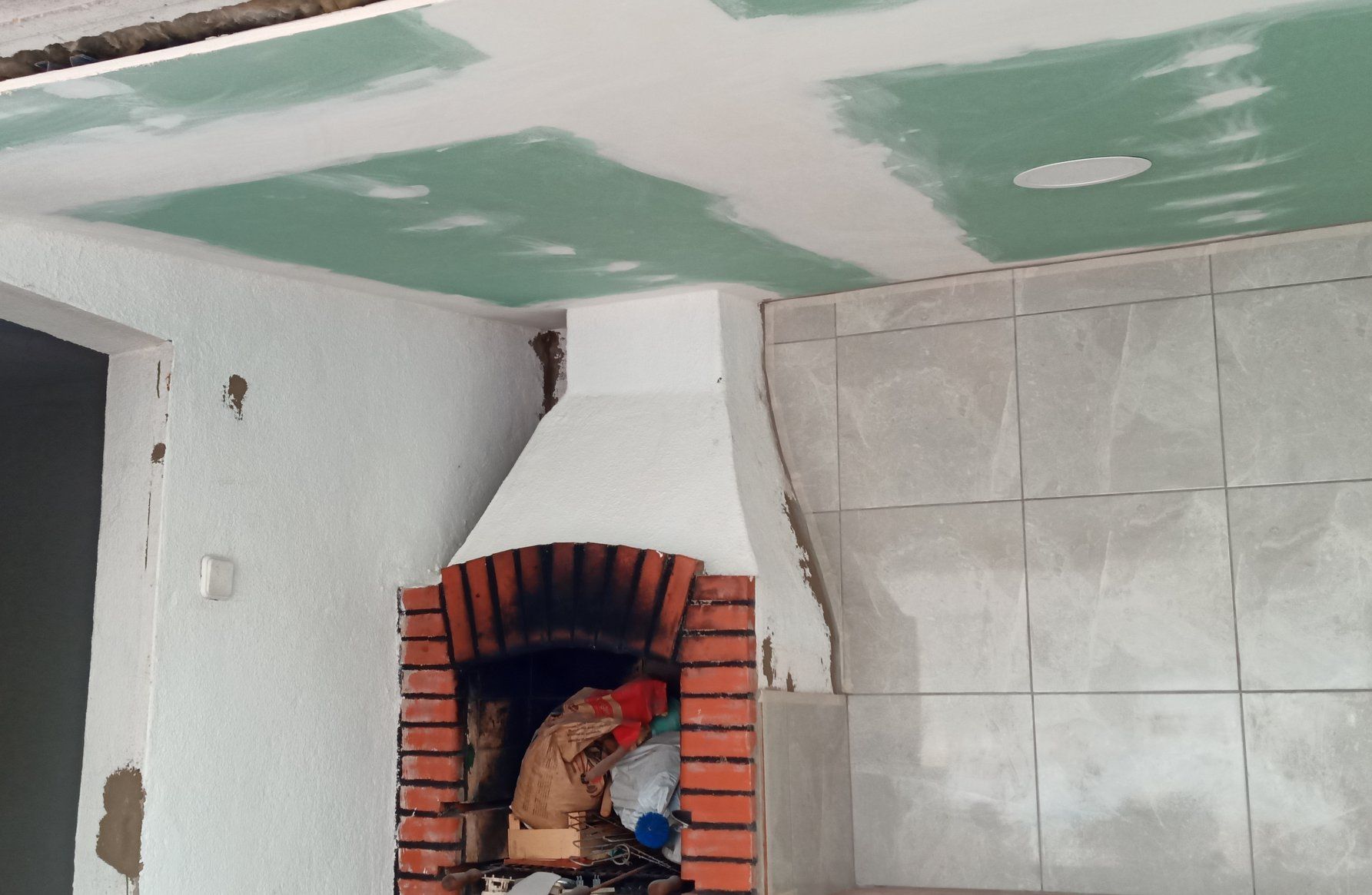 Lareira de tijolos com paredes de gesso branco, parede revestida com azulejos e teto de gesso verde.